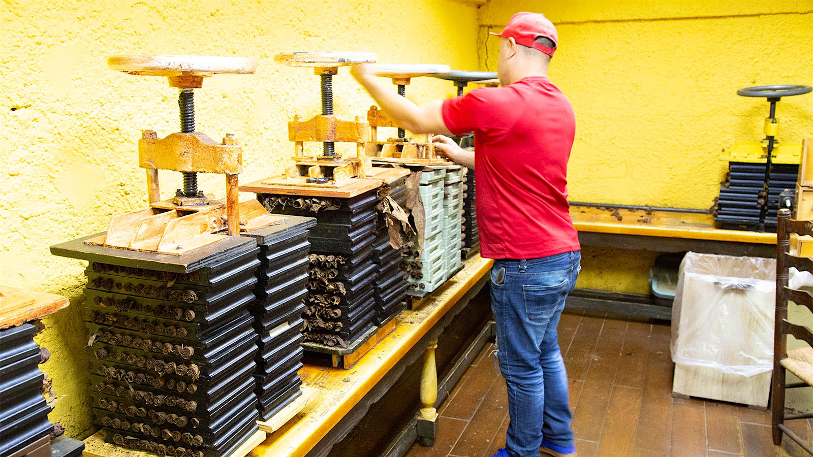 A factory worker loosening a vice before rotating the cigars inside the molds that are being compressed.