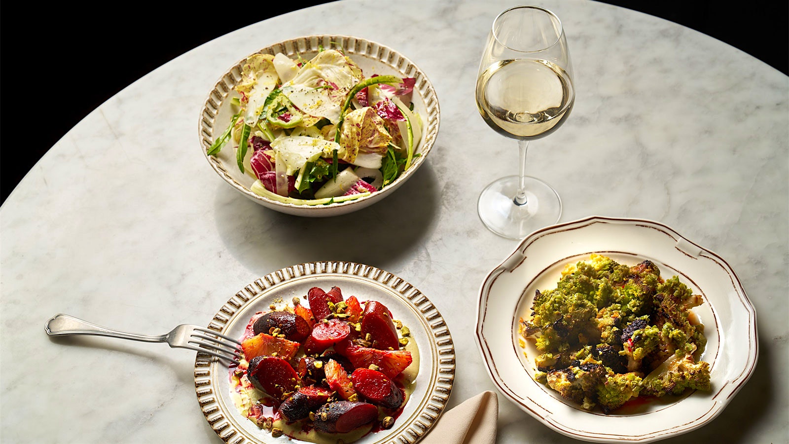  A table of vegetable dishes from Sempre Oggi like chicory salad, roasted beets and romanesco with a glass of white wine.