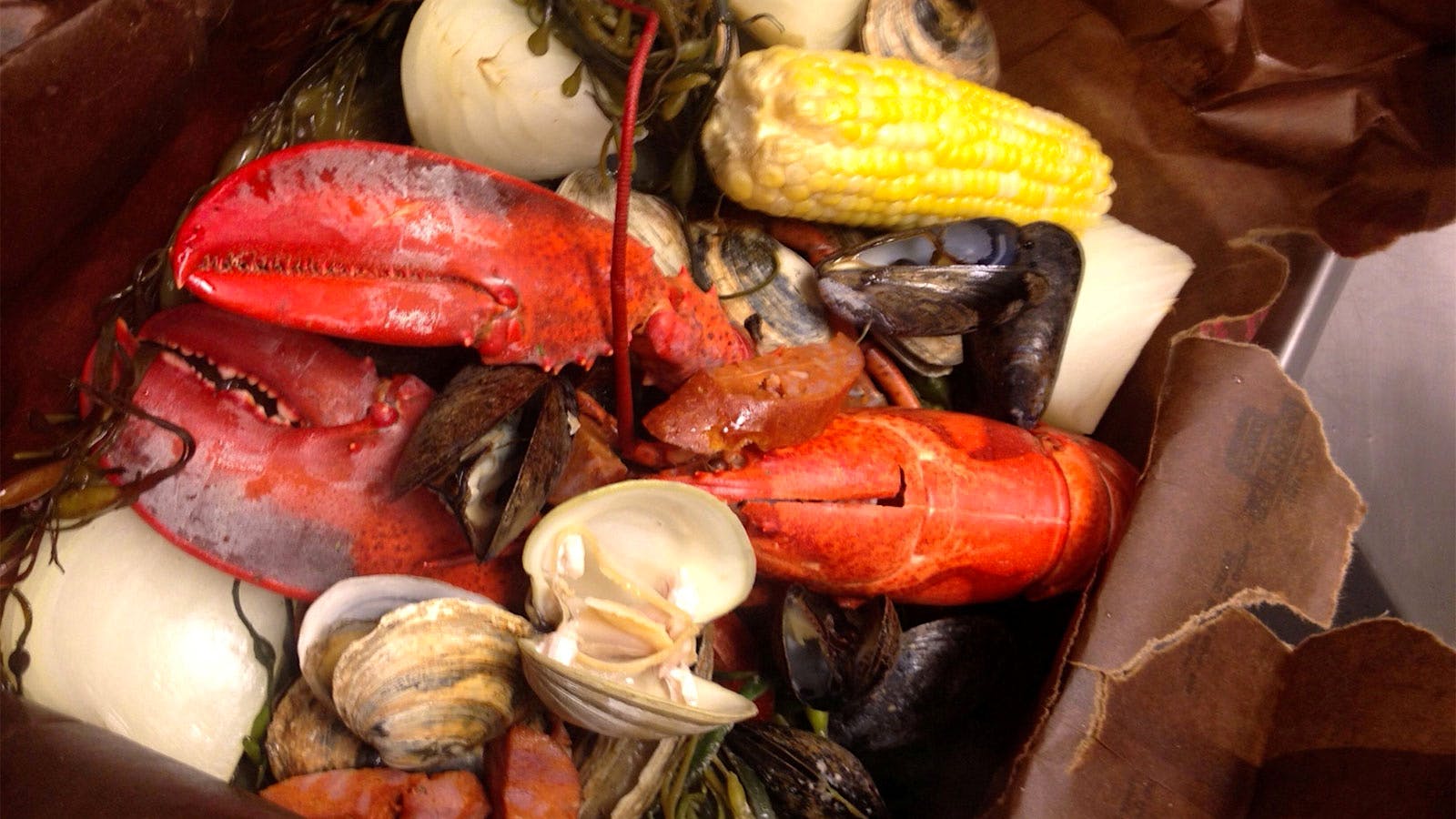 Lobster, clams, sausage, corn and potatoes bake together in a paper bag.