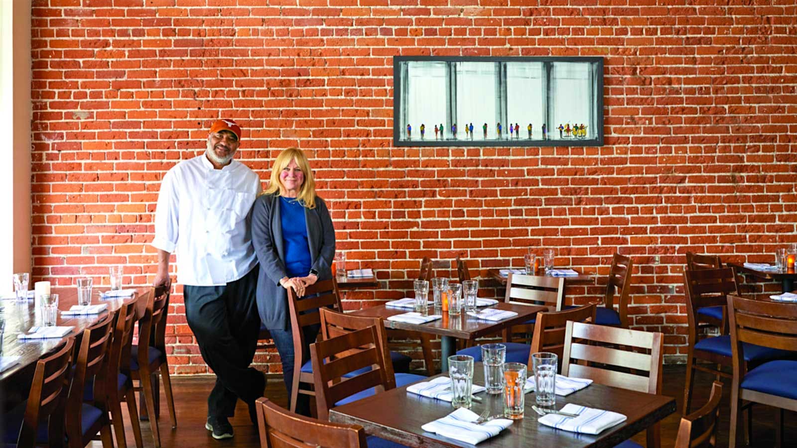 The two owners standing in front of a brick wall in their restaurant