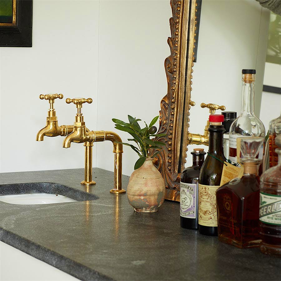A wet bar with sink, brass-colored fixtures, an ornate mirror and liquor bottles. Photo by Ty Cole