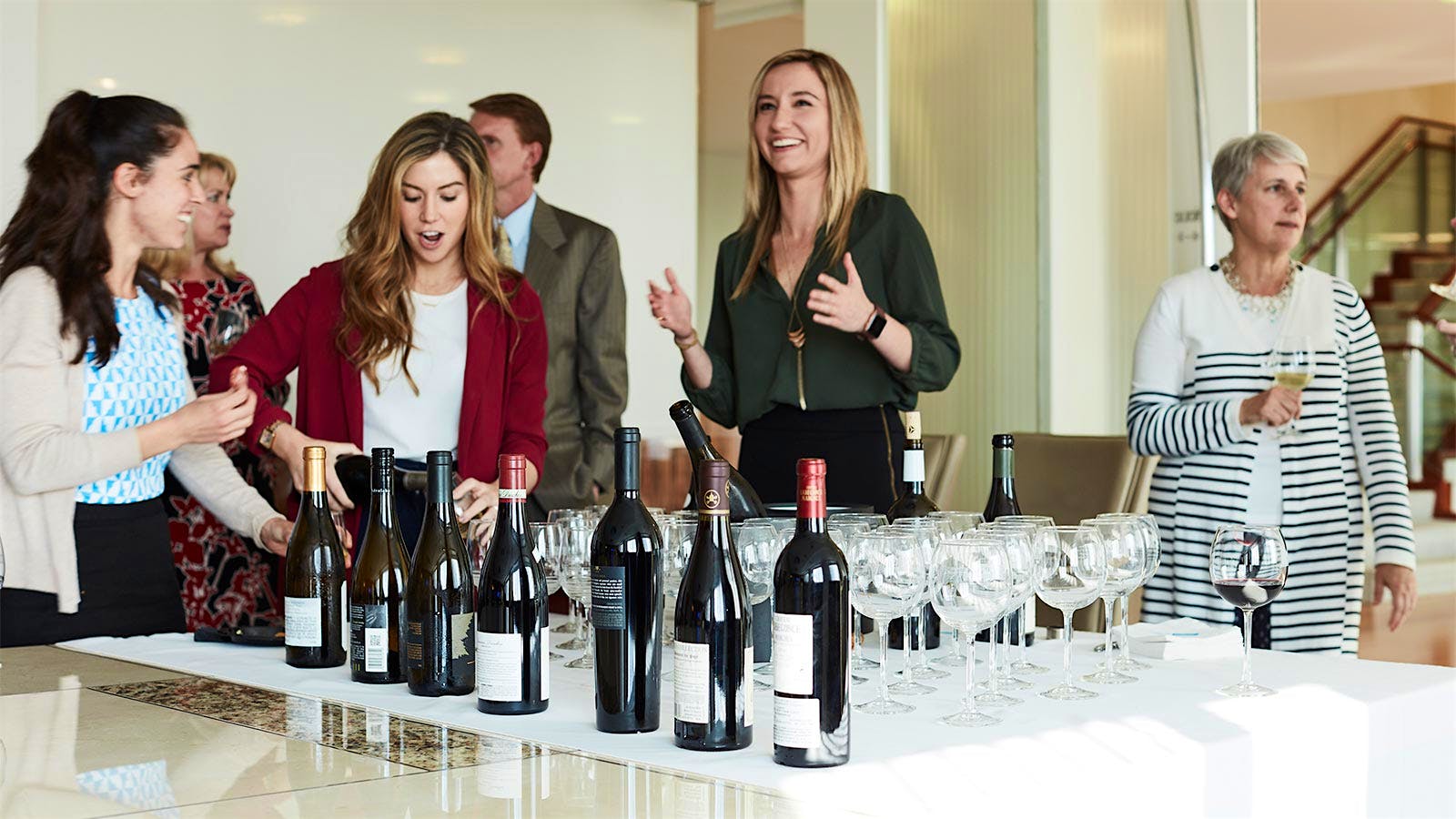 Group of law firm employees gathered for a wine tasting, with bottles and glasses on a table.