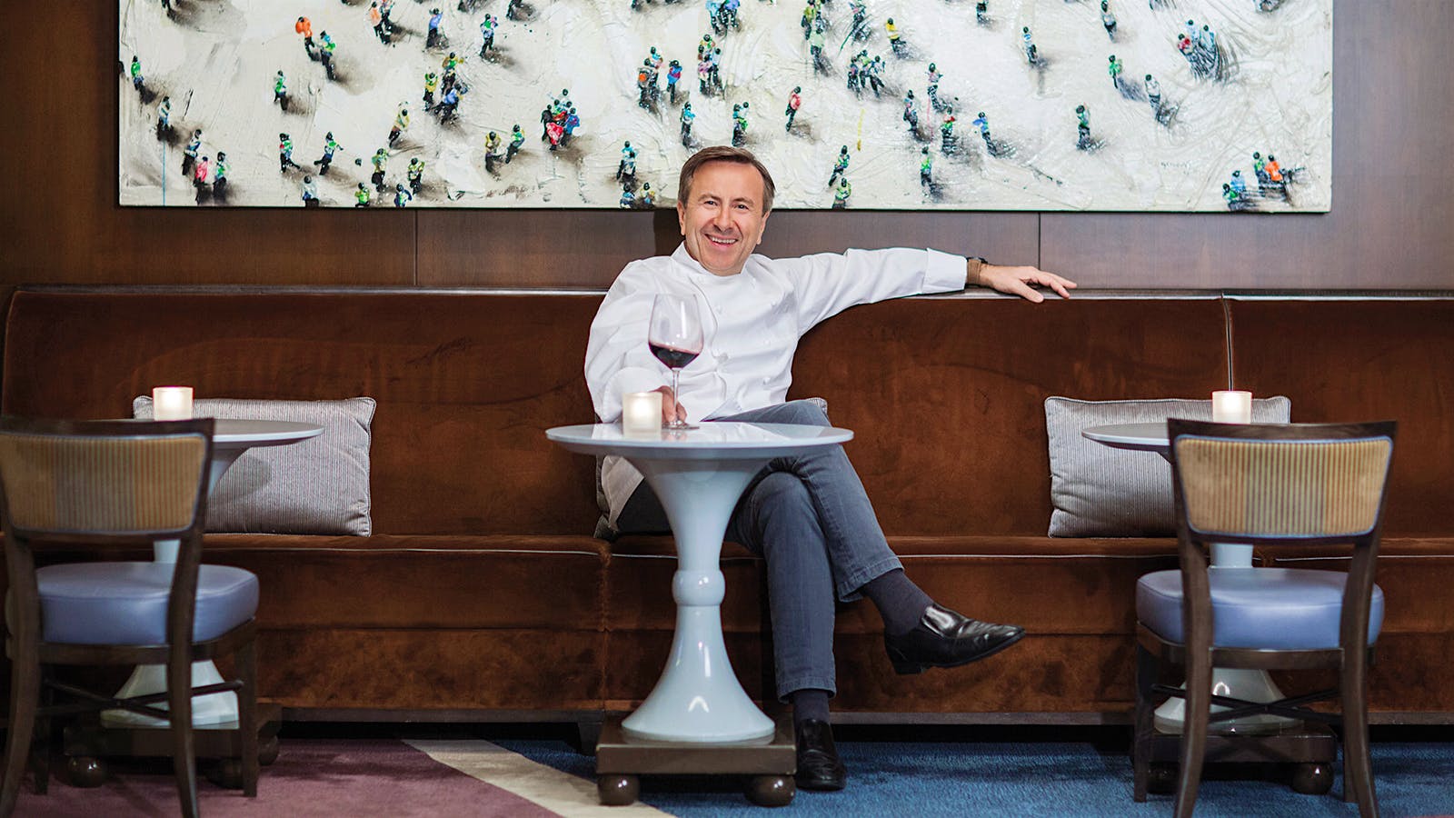 Chef Daniel Boulud at a table in his restaurant with a glass of wine