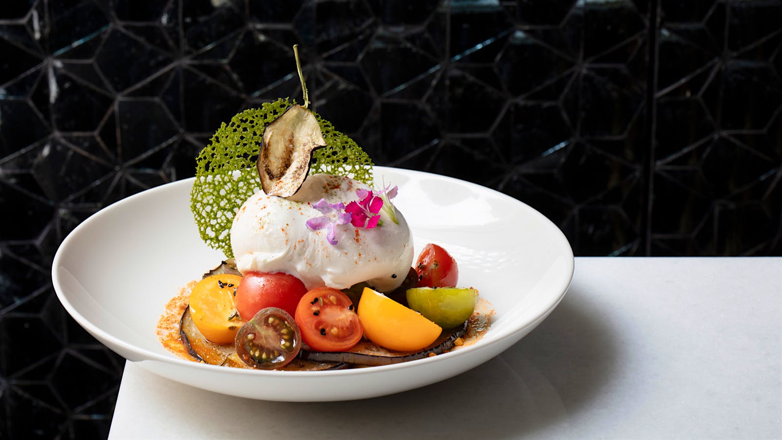 Burrata with eggplant and tomatoes on a white plate against a black background