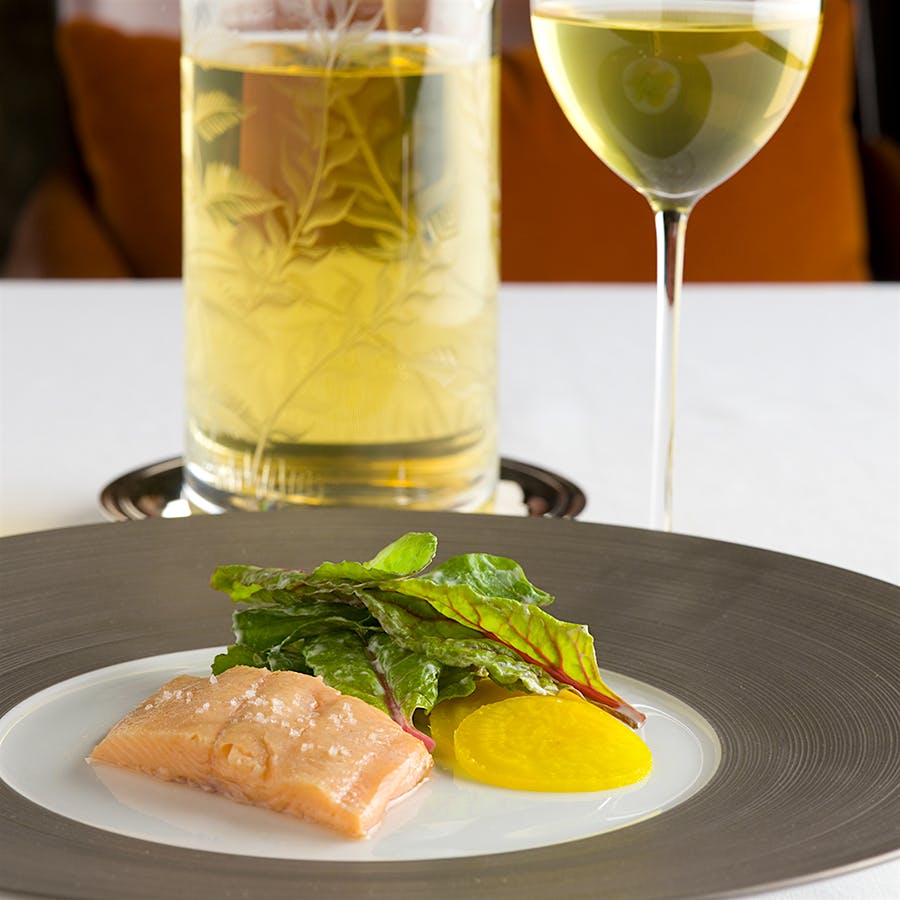 Appetizer of smoked trout with yellow beets and greens, accompanied by a glass and carafe of white wine