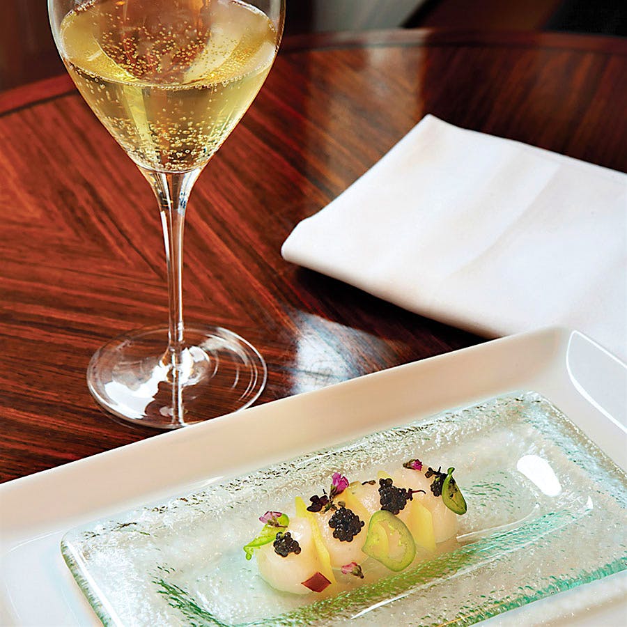 A glass of Champagne with a small plate of scallop crudo with caviar, jalapeño and apple