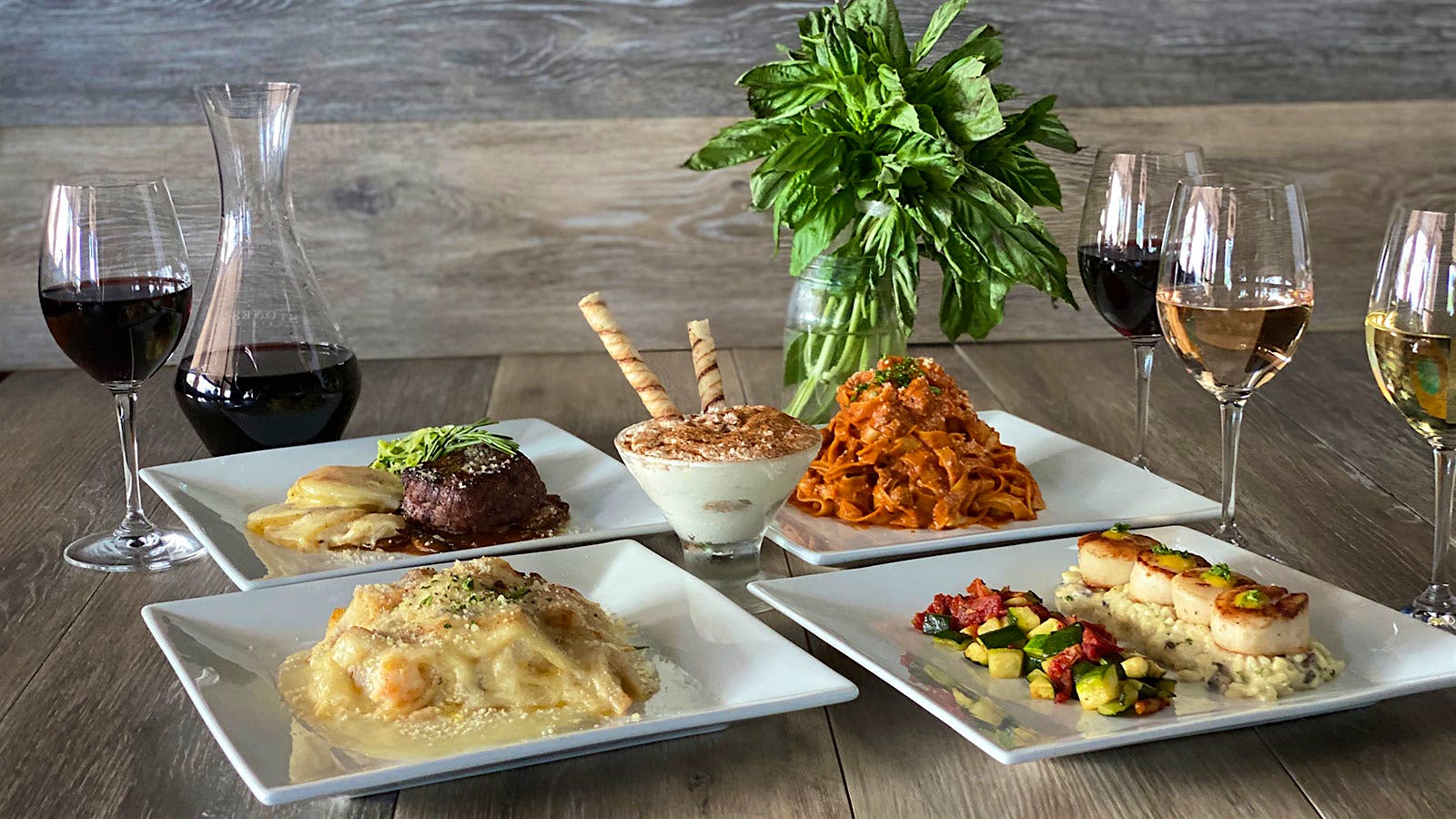 Four entrées and a dessert from the Grove Pizza Cucina & Wine Bar, next to a decanter of wine with a few glasses poured