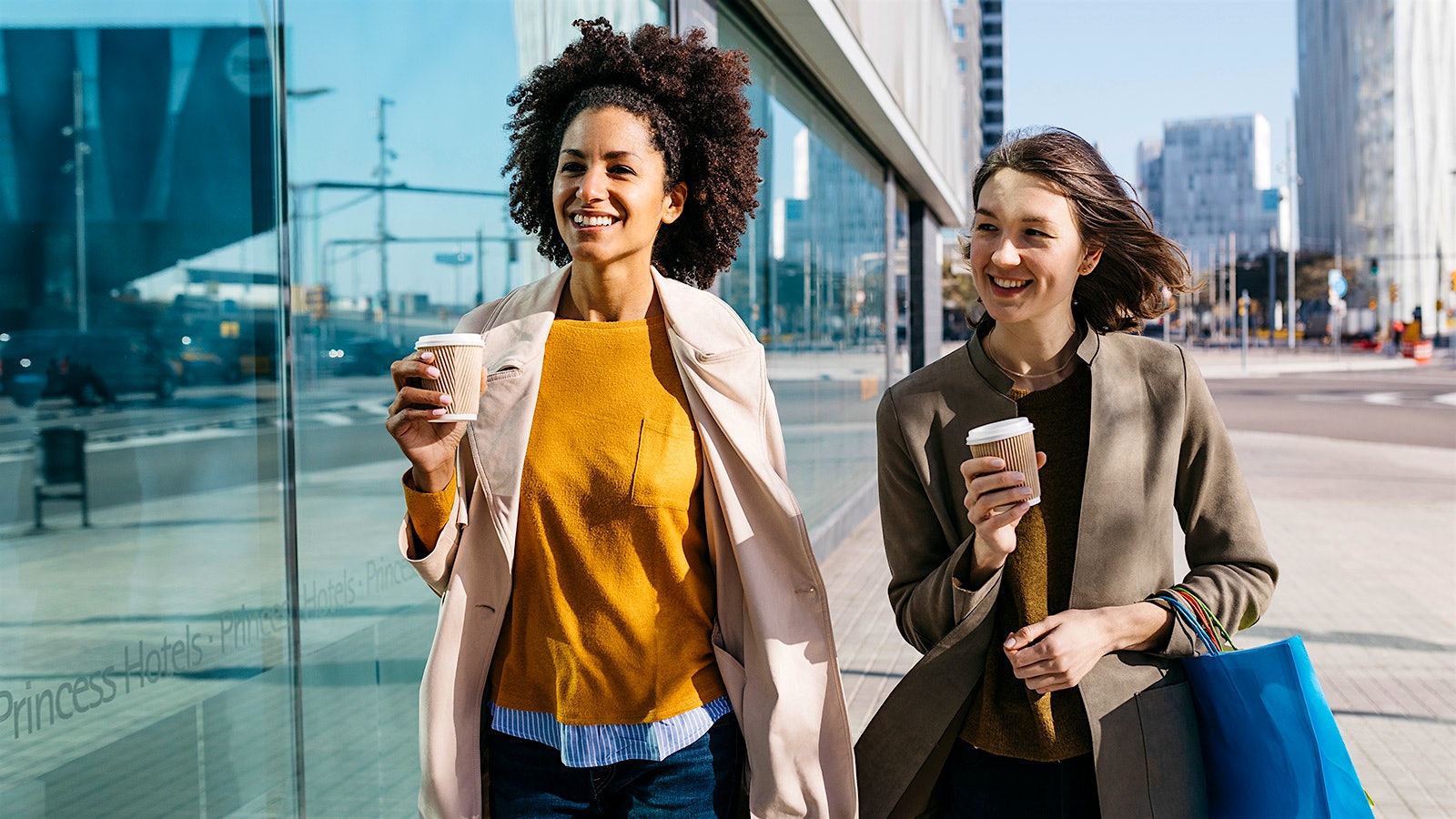  Two women drinking coffee while walking in a city