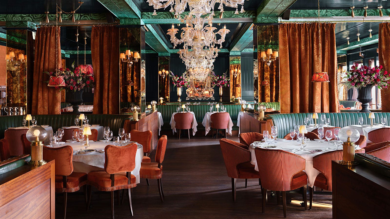 The dining room at Carbone Miami, with a green ceiling, velvet and striped red chairs, brown curtains and chandeliers