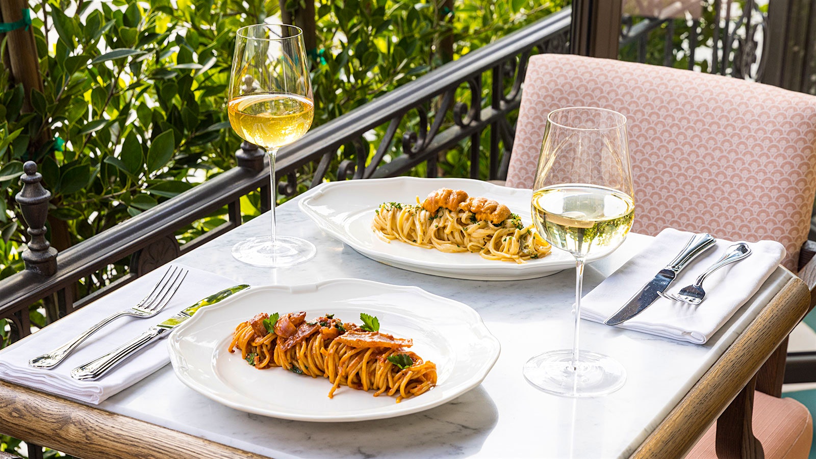  Plates of pasta and glasses of wine on a table on the foliage-surrounded terrace at the Restaurant at the Georgian