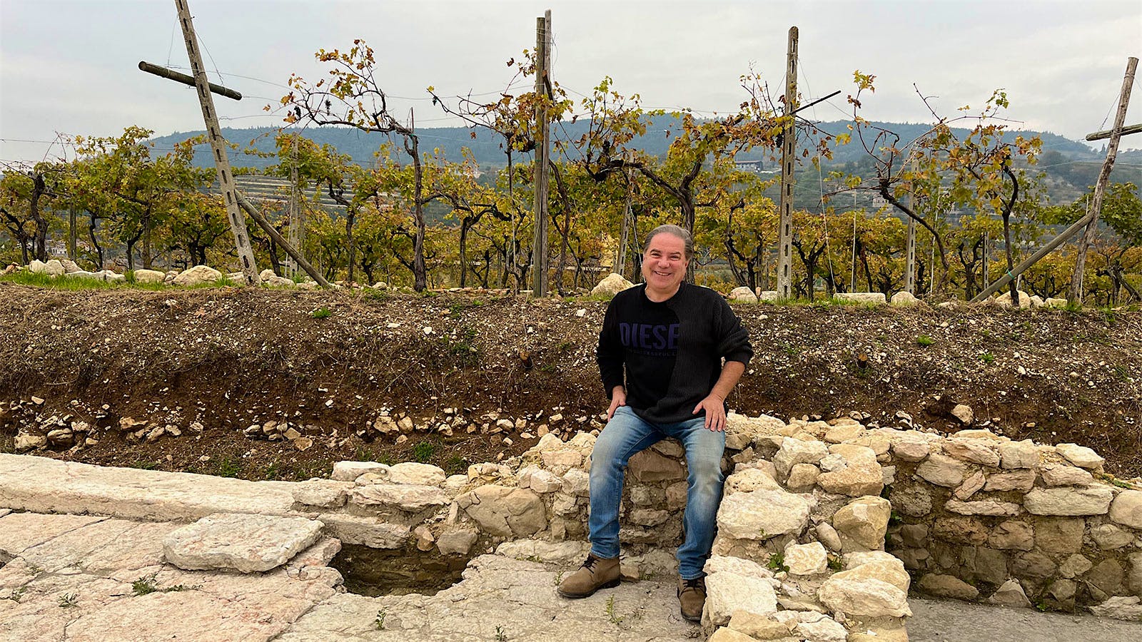 Winegrower Giuliano Franchini sits on the stone wall of an ancient Roman villa bordering rows of grapevines