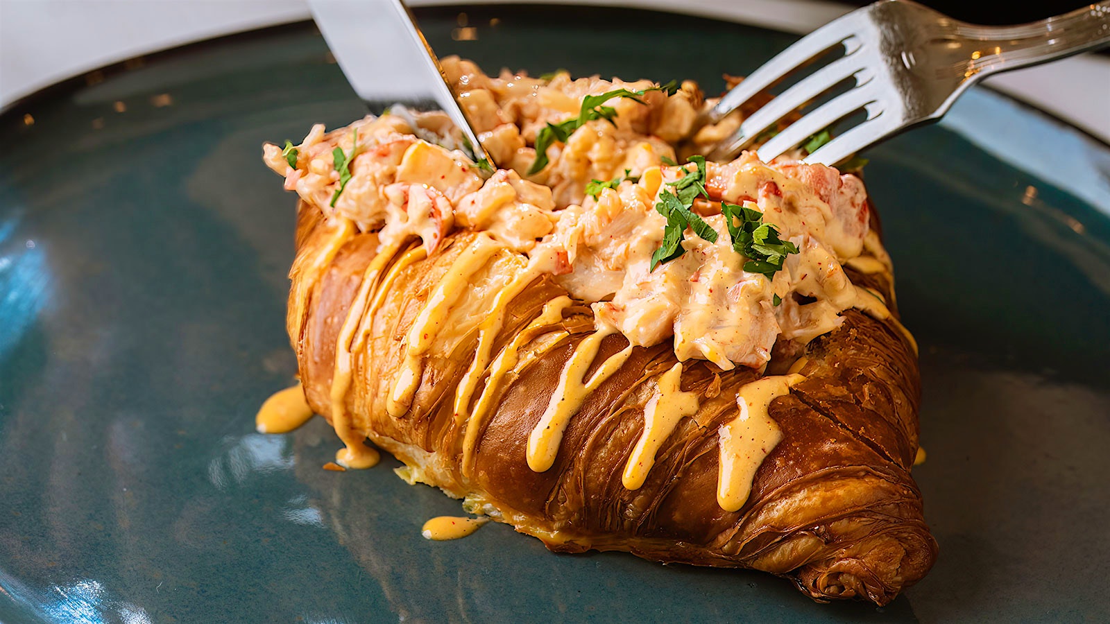  A diner cutting with a knife and fork into a croissant filled with a Maine lobster salad