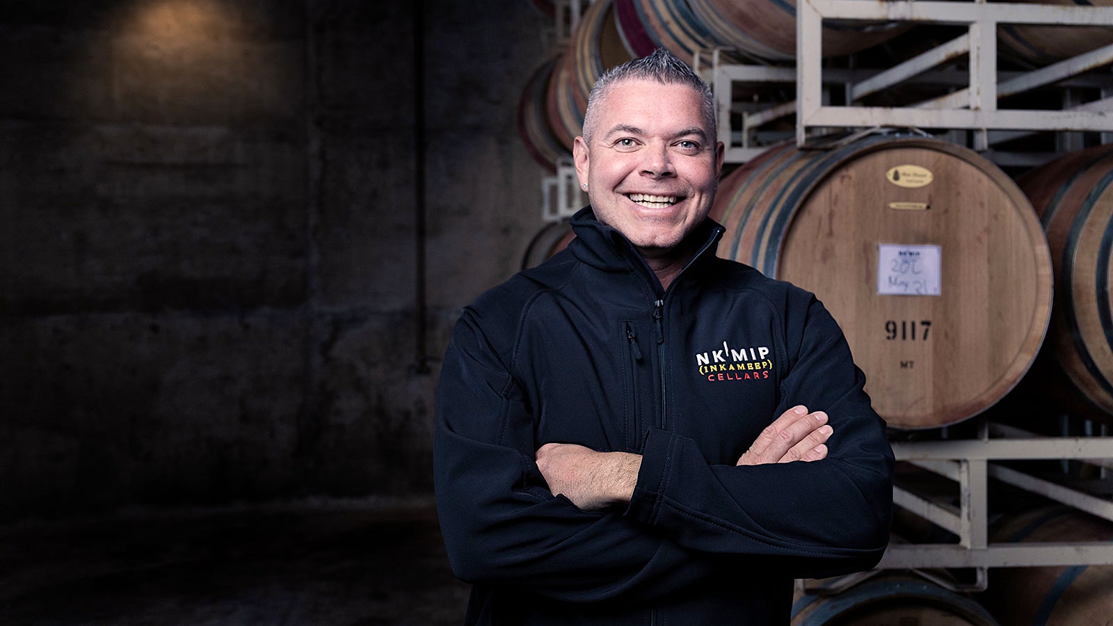  Portrait of Nk'Mip winemaker Justin Hall in front of a stack of wine barrels