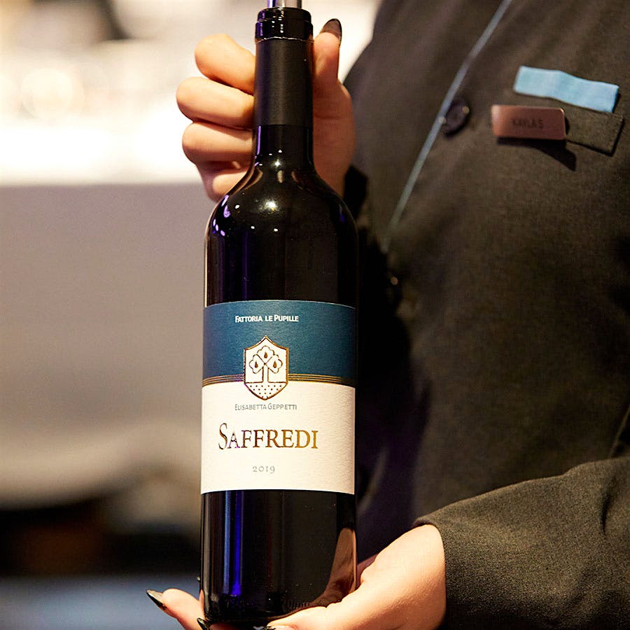  A Wine Experience staff member holding a bottle of Fattoria Le Pupille's 2019 Saffredi