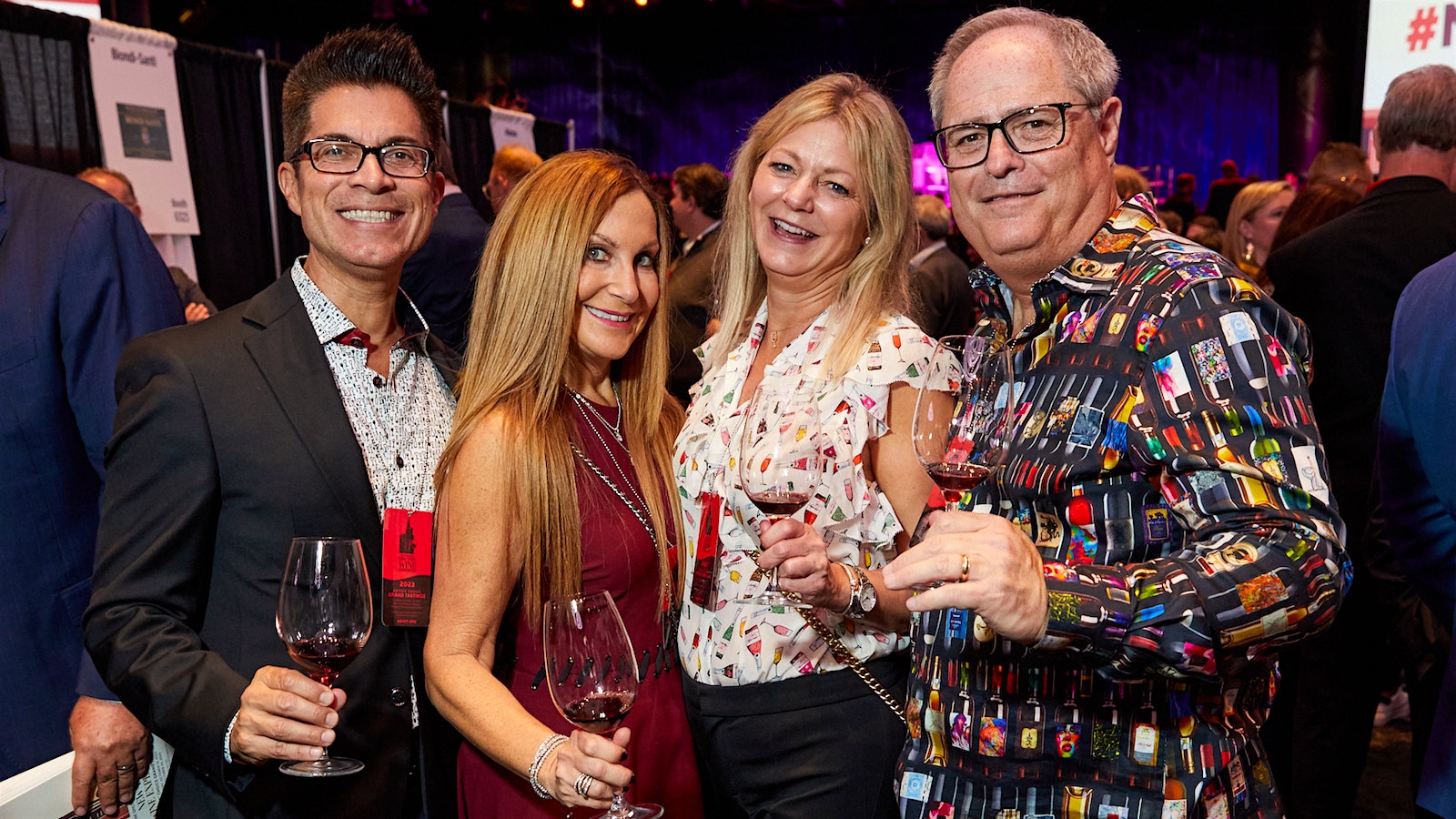  Two women and two men, with three in the group wearing wine-themed shirts, attending the Wine Spectator Grand Tasting together