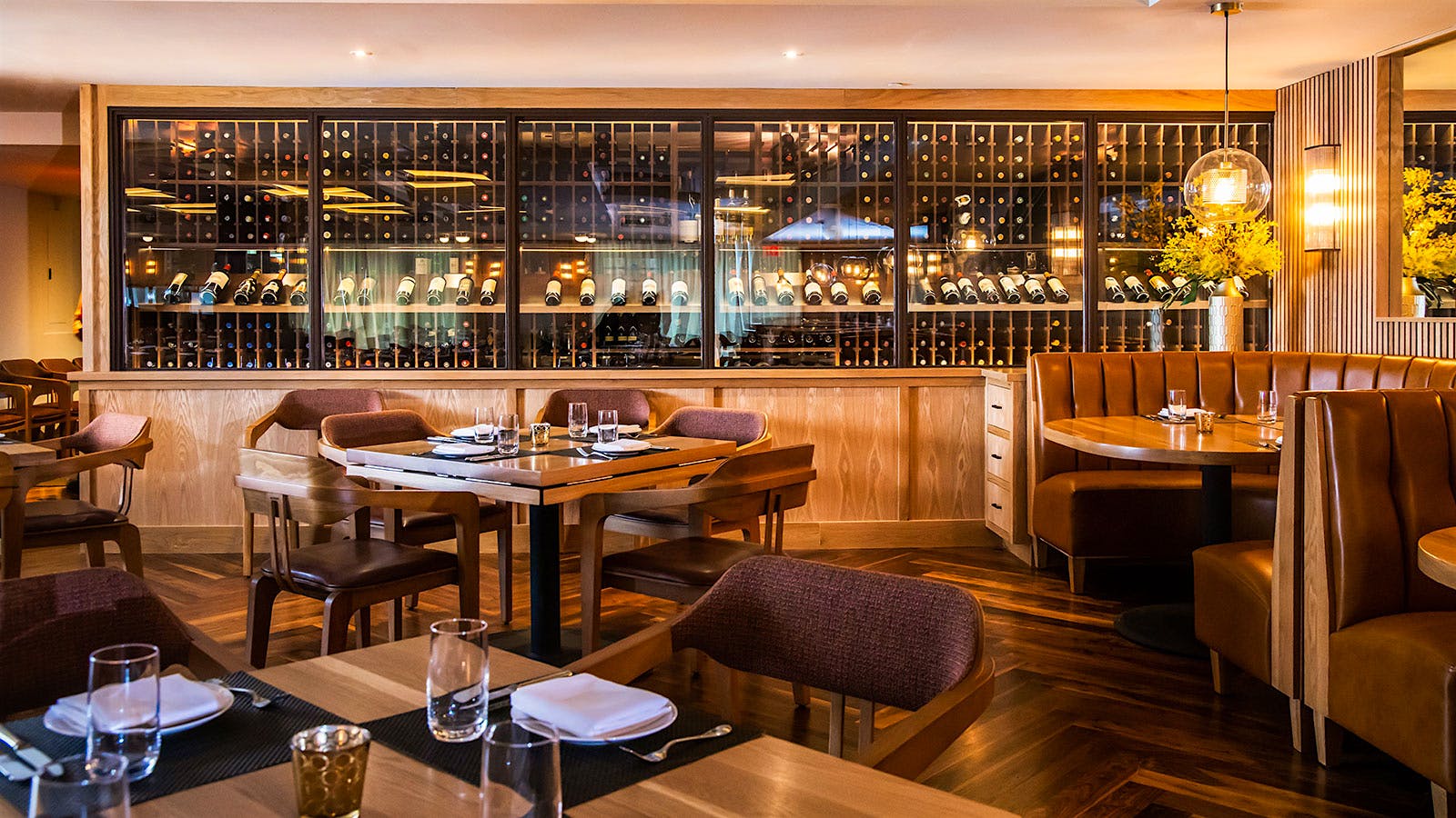  Wood tables and chairs made of wood and red cloth in front of a glass-paneled collection of wine bottles on racks in the dining room at BLT Steak in Washington, D.C.
