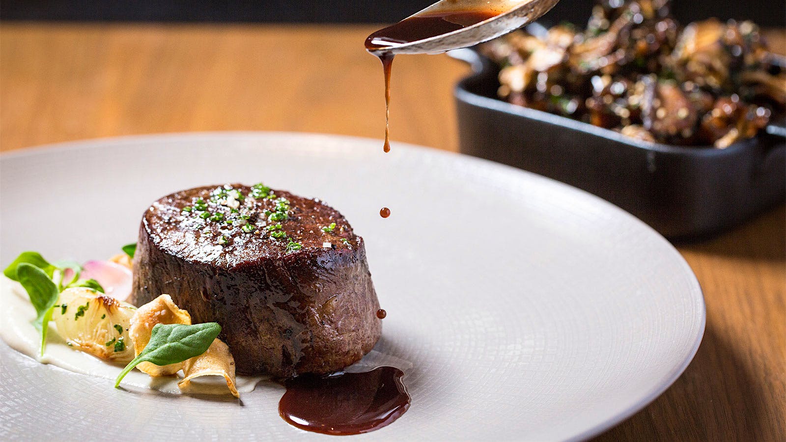  A filet mignon on a plate being dressed with brown steak sauce at Seattle&rsquo;s Bourbon Steak