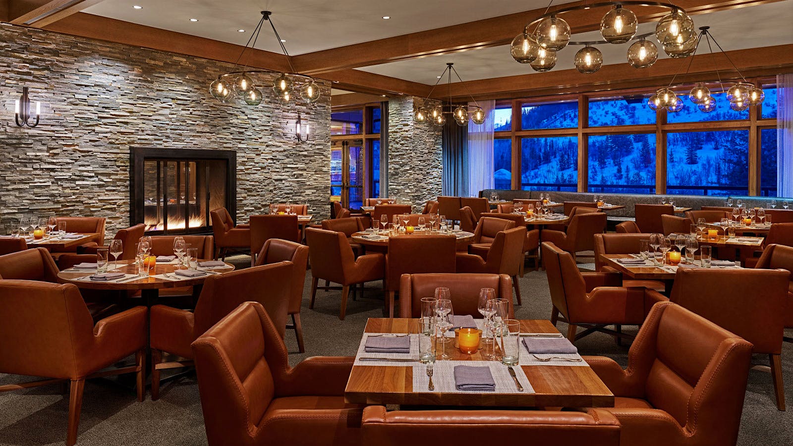 The dining room at Rime, with a stone wall, a fireplace, red leather chairs and a window view of a snowy mountain