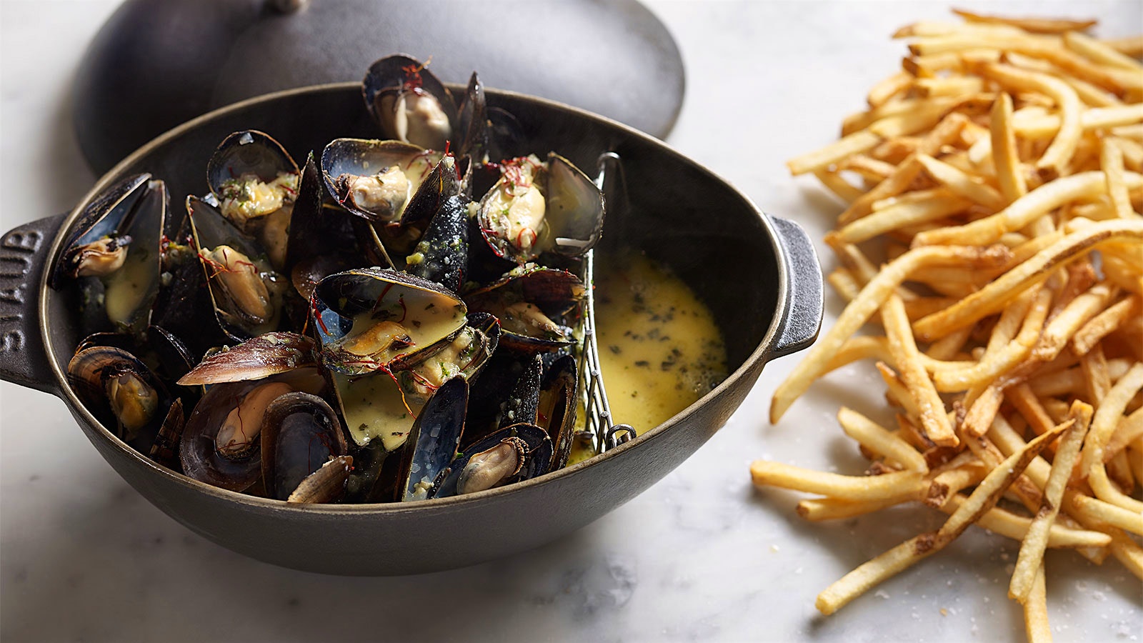  Mussels in a cast-iron bowl next to French fries at Bouchon Bistro in Coral Gables, Florida