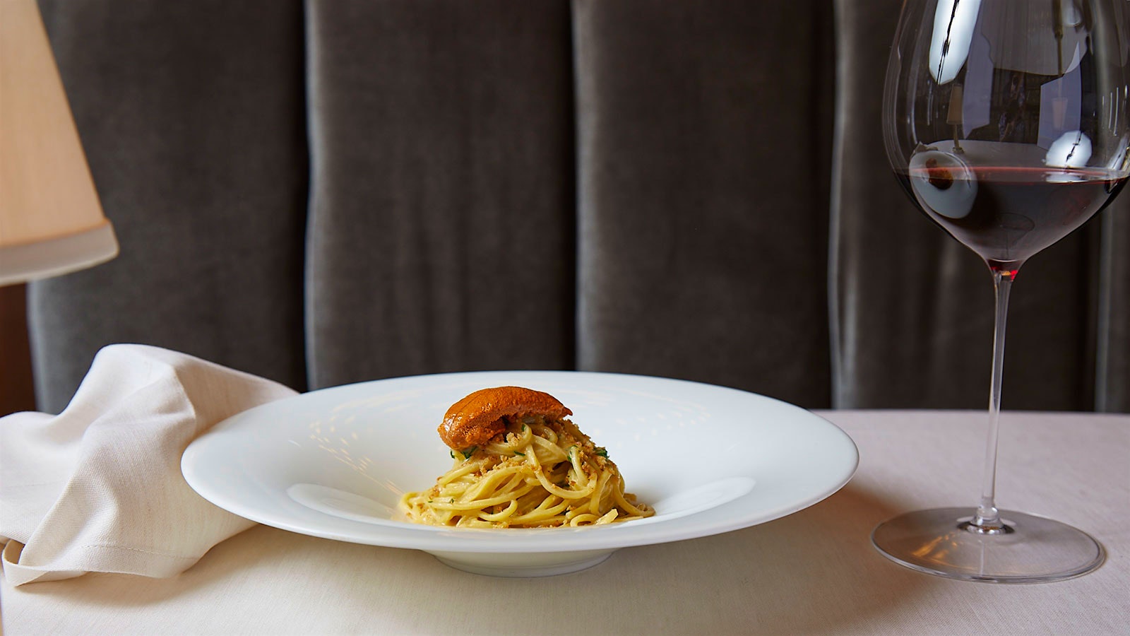  A plate of spaghetti with sea urchin, garlic, lemon and pepperoncini next to a glass of red wine at Four Twenty Five in New York City