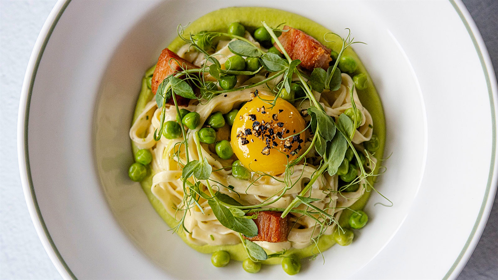  A nest of spaghetti carbonara with green herbs, peas and a golden egg yolk.