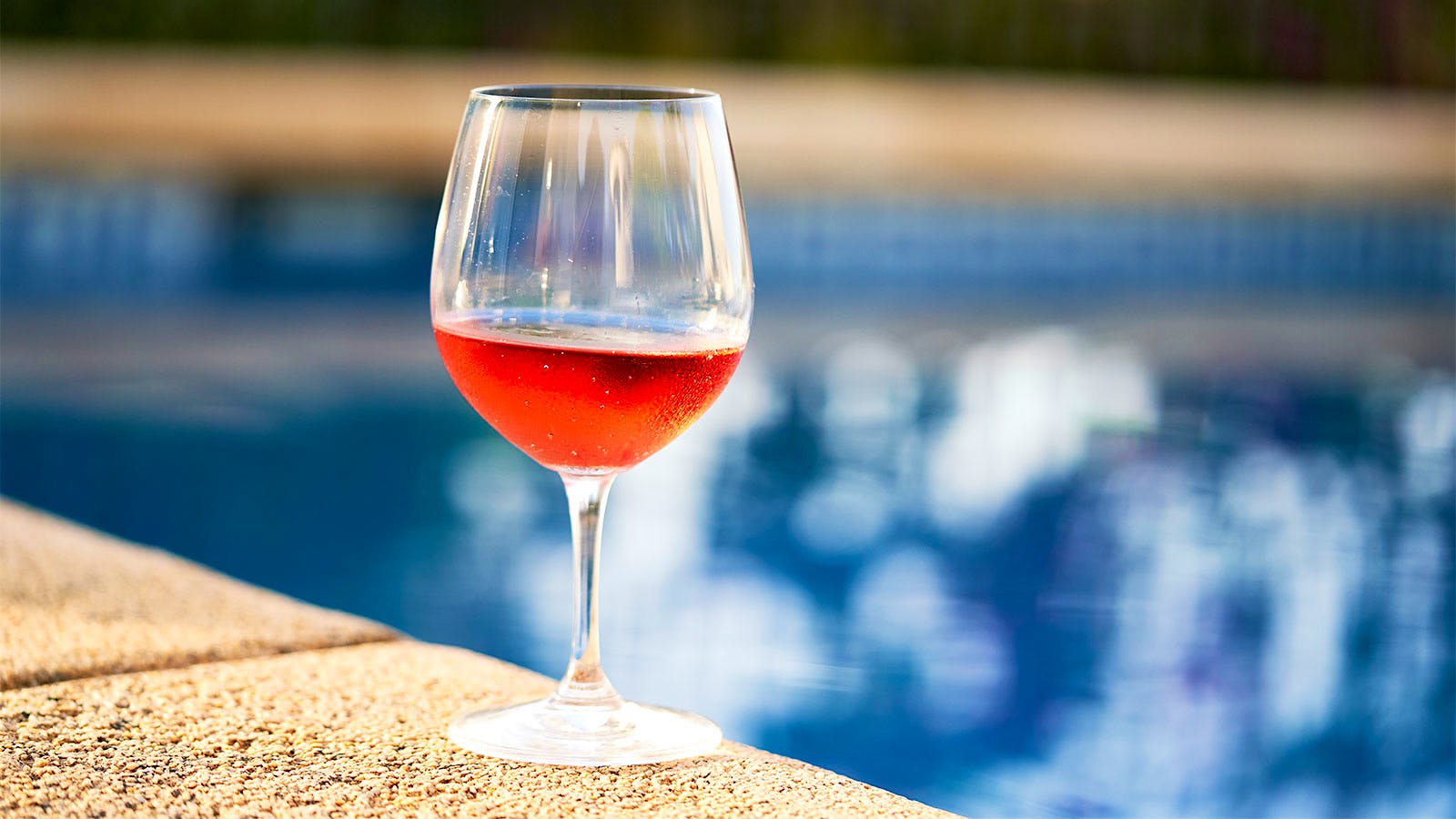 A glass of rosé sitting on the side of a swimming pool