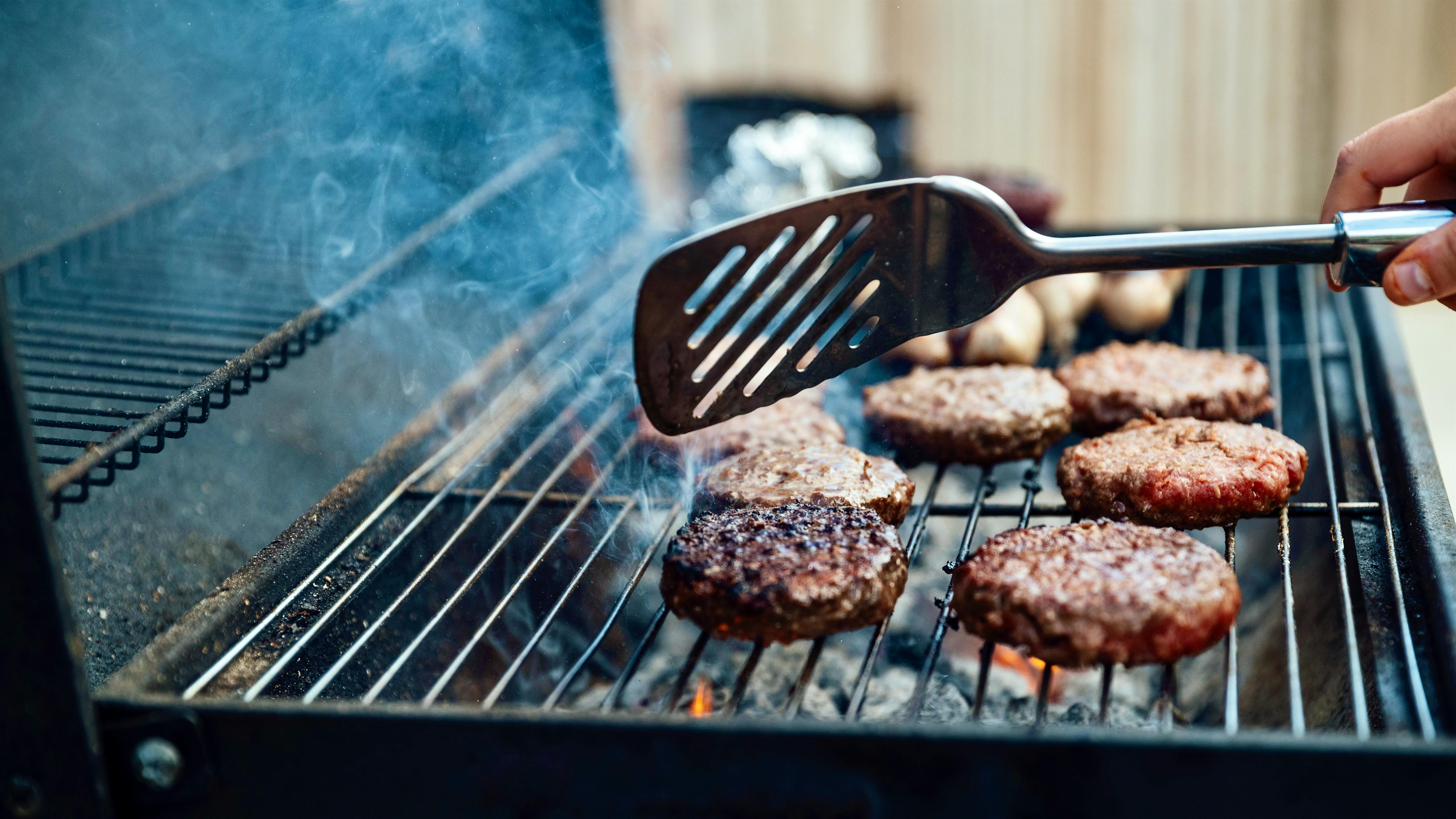 A person flips burgers on an open grill