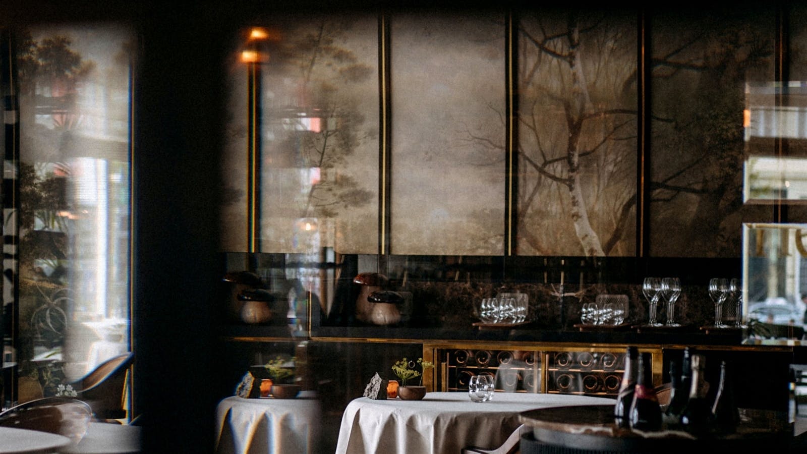 The dining room of Restaurant Flore in Amsterdam, with walls decorated with a painting of a forest and a Champagne bucket in the center.