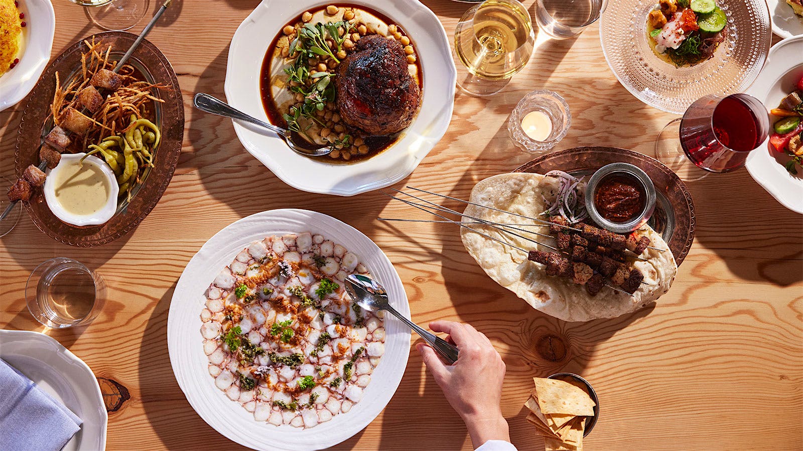 A spread of dishes and wine glasses at Dalida, including lamb shoulder and octopus carpaccio.