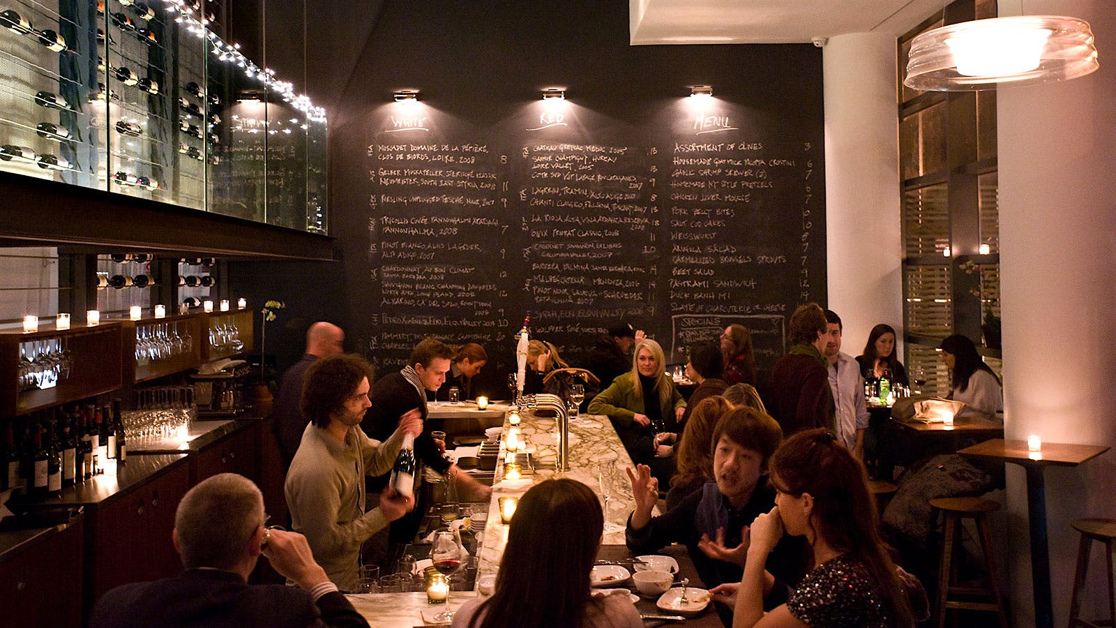 People dining at the bar of Ardesia in Hell's Kitchen, Manhattan, where wine and menu items are written in chalk on a chalkboard wall