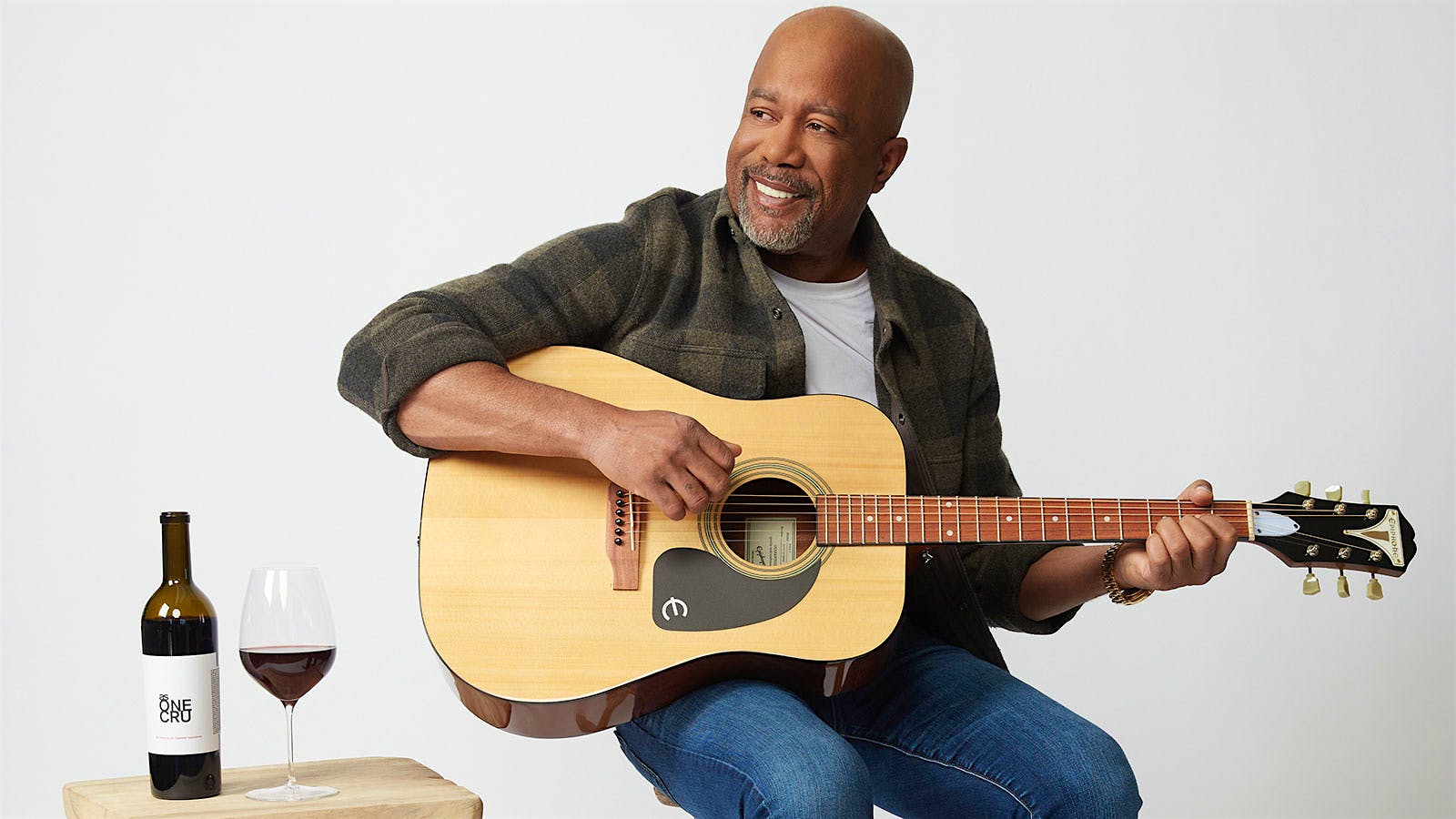 Singer and songwriter Darius Rucker playing a guitar alongside a glass and bottle of As One Cru Cabernet Sauvignon red wine