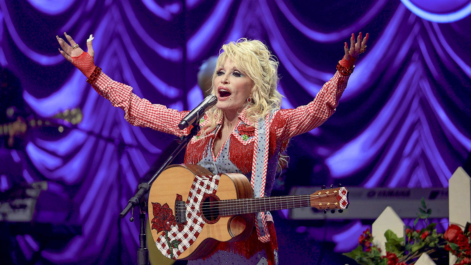 Singer and songwriter Dolly Parton, with arms raised, on stage with a guitar