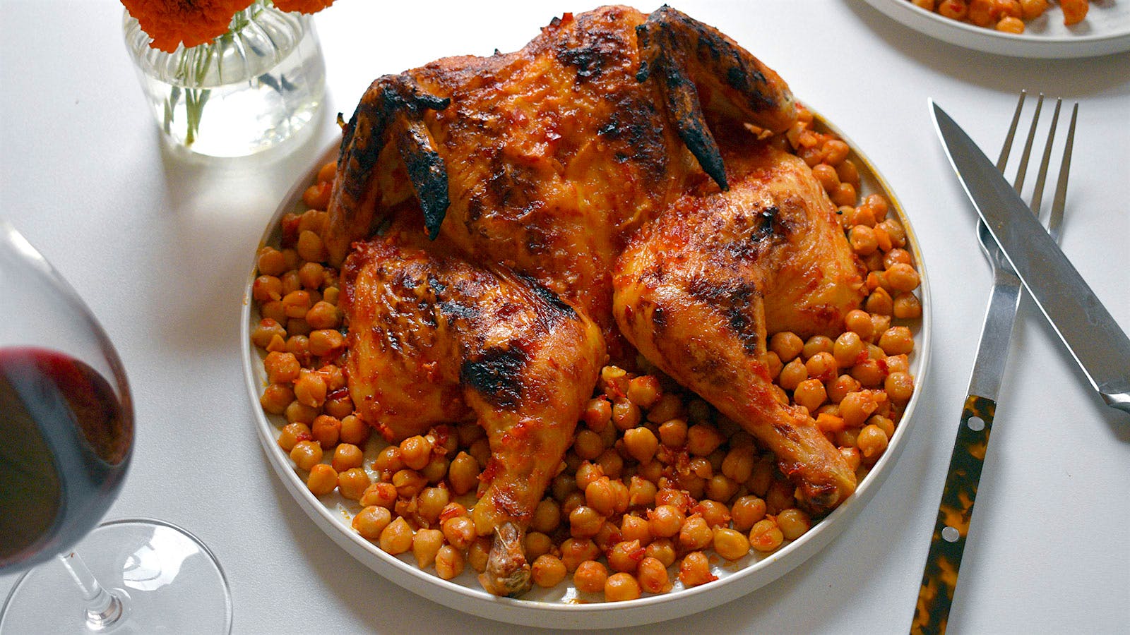 A roasted chicken with harissa and chickpeas, next to a glass of red wine