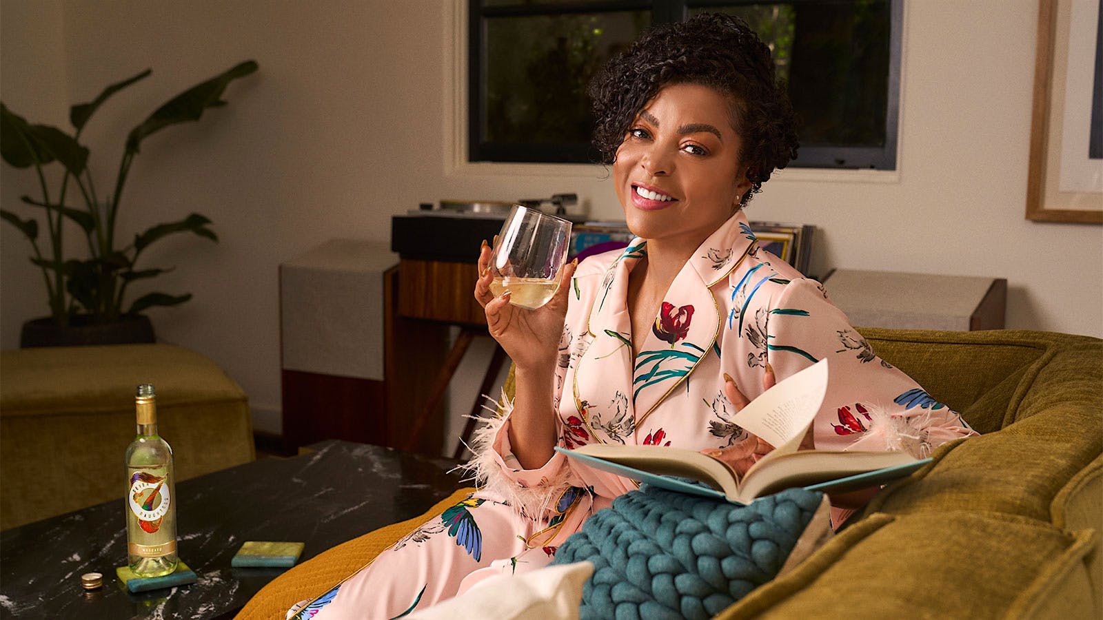 Taraji P. Henson on the couch with a glass of Moscato wine and a book.