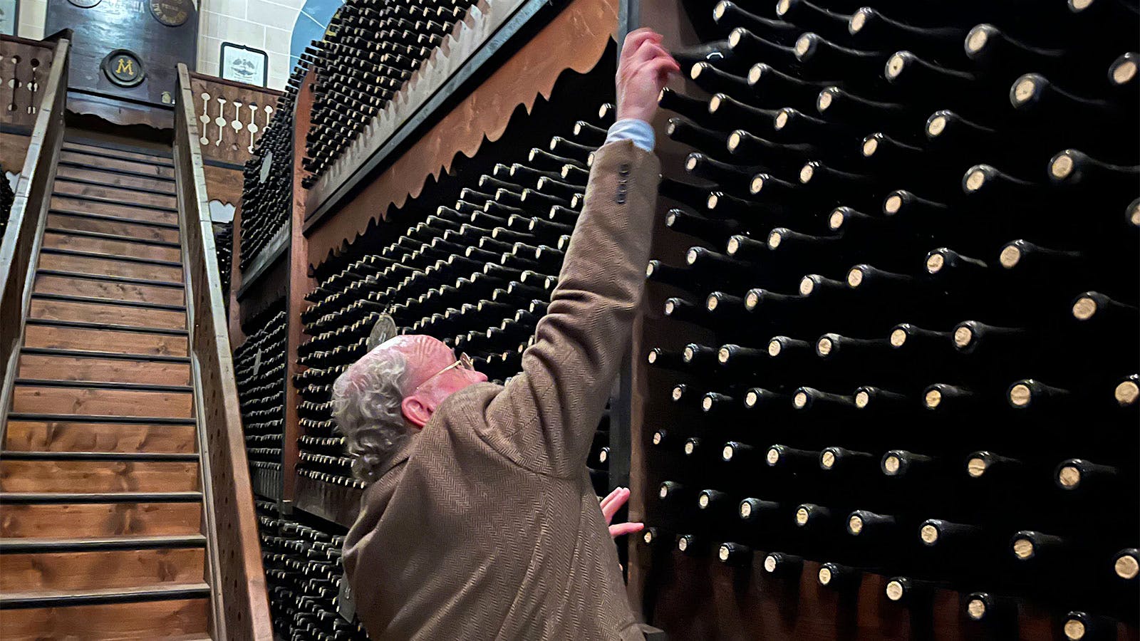  Baron Arnaldo Spitaleri reaches for a bottle of wine high up on a wooden storage bay next to a set of steep wooden stairs