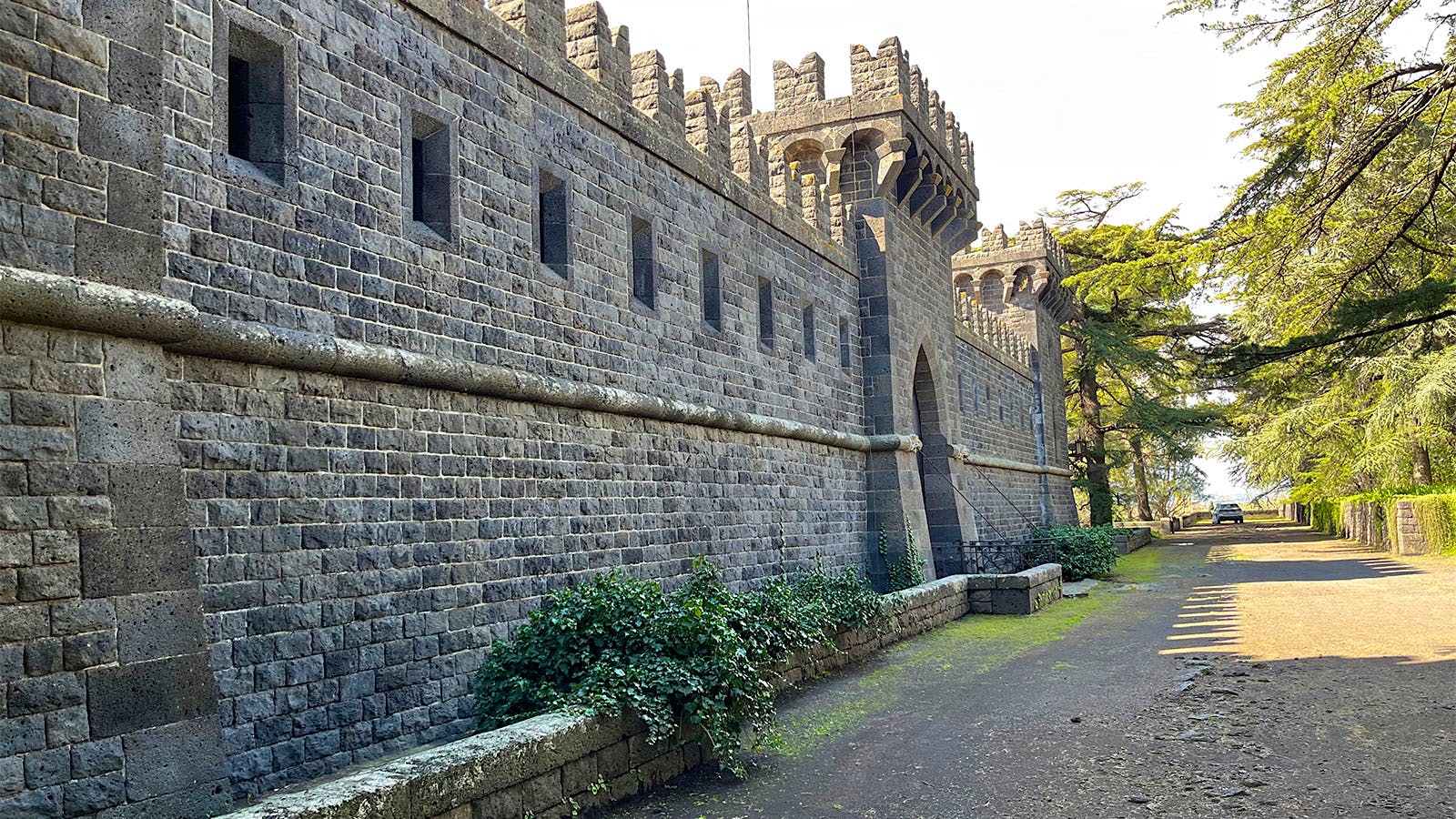  A close view of one of the Castello&rsquo;s thick, tall walls, built from gray and black Mount Etna lavastone, with wooden gate and turret