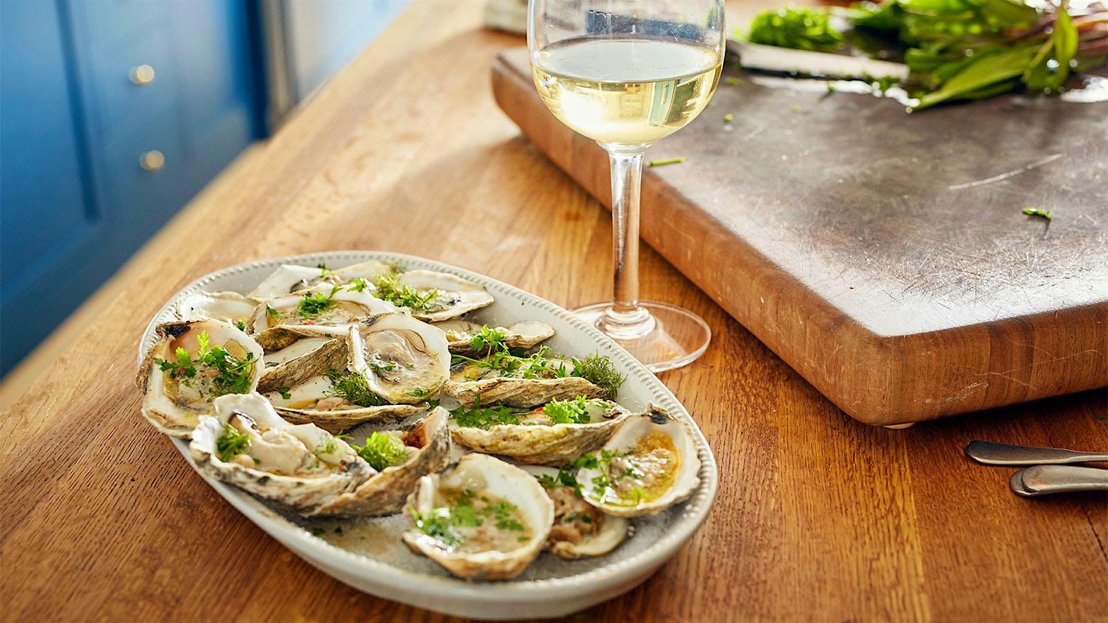  Grilled oysters with lemon chile ramp butter next to a cutting board and glass of white wine