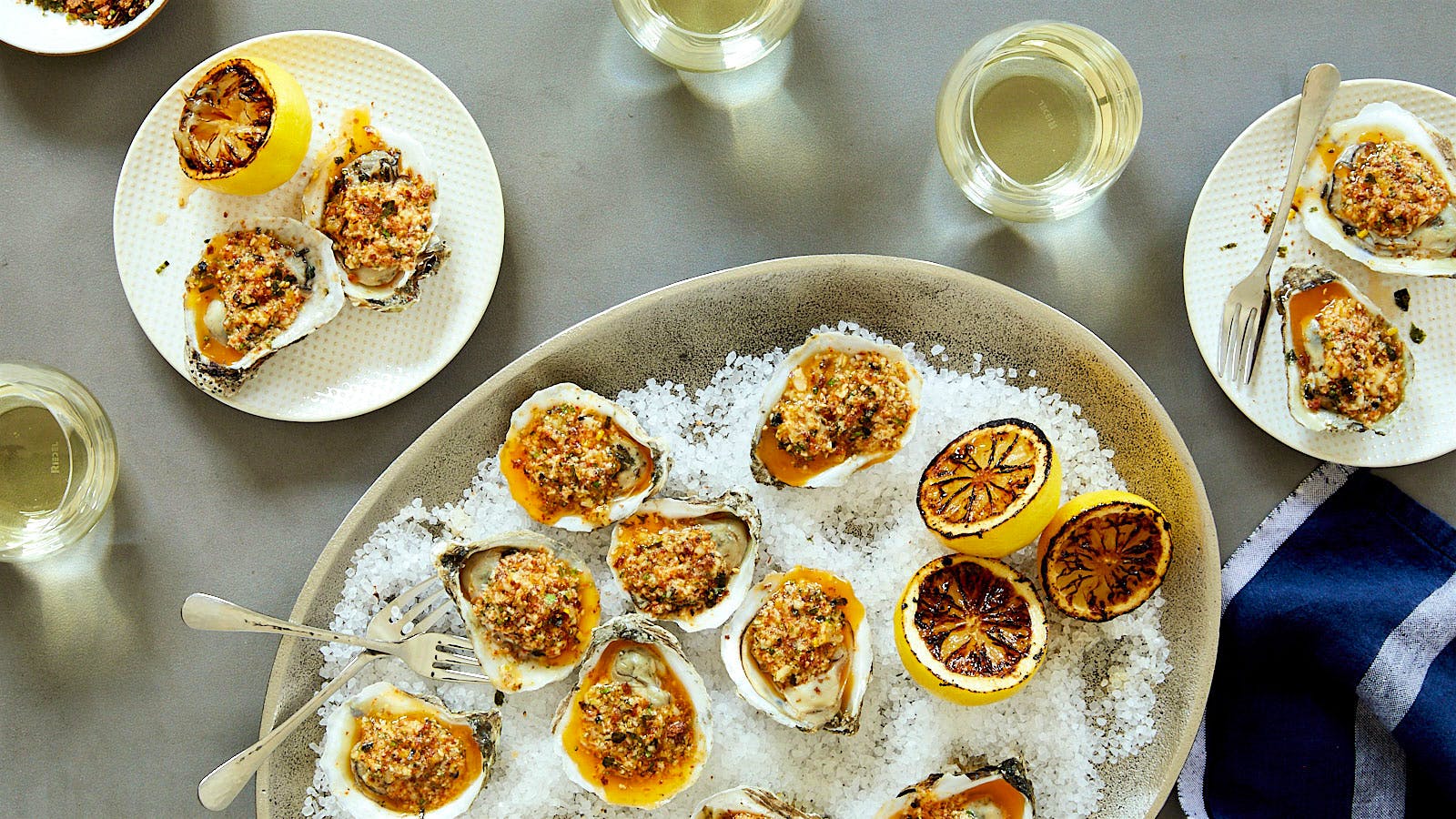  Roasted oysters with citrus garlic butter on a bed of salt served with glasses of white wine