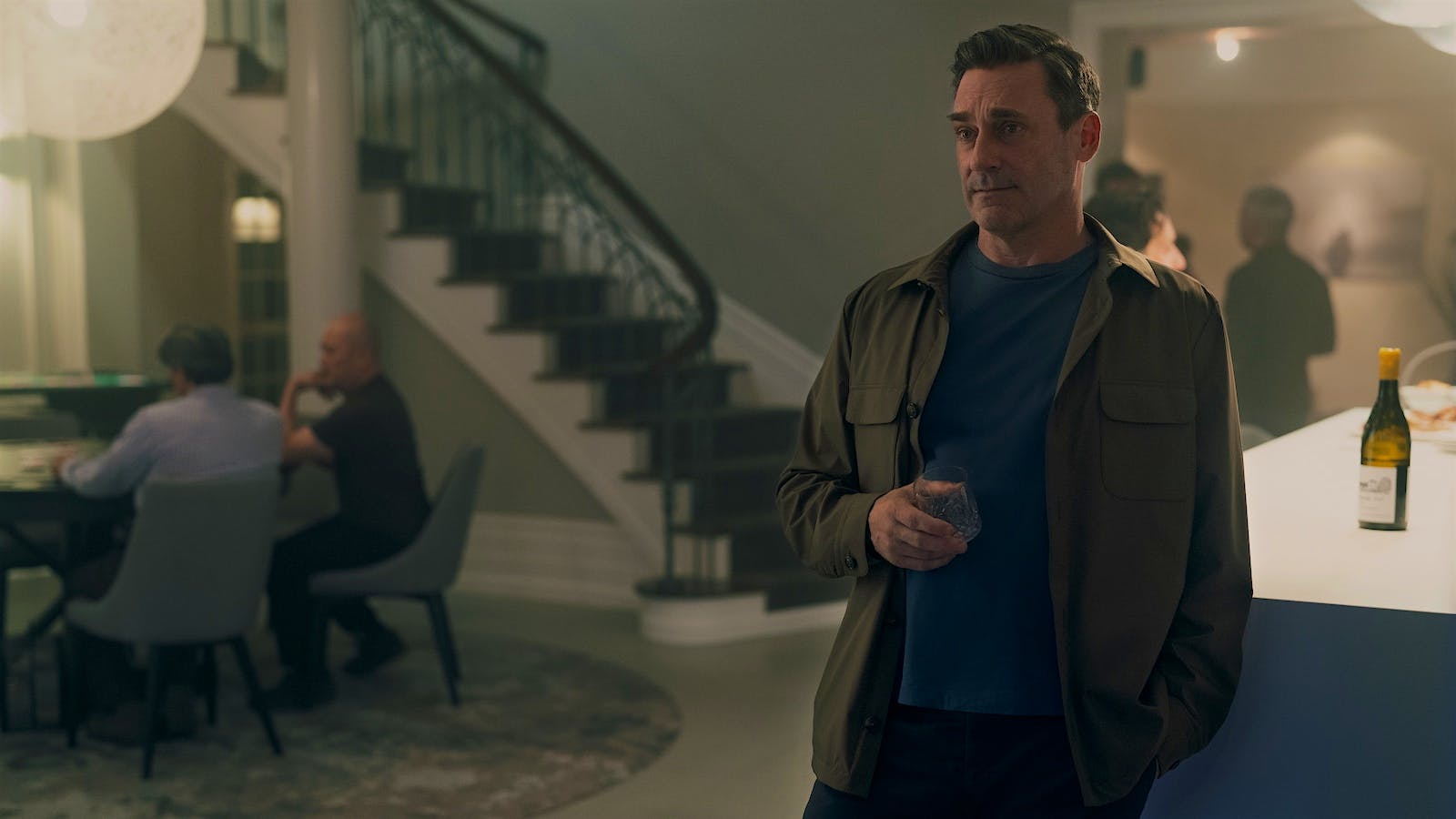 Jon Hamm, playing Coop in Your Friends & Neighbors, holds a glass of white wine at a party