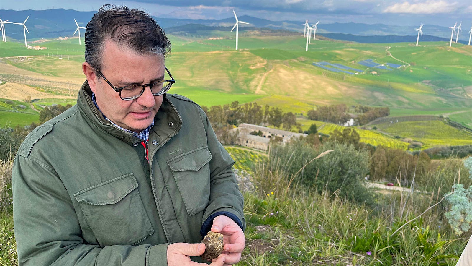  Fabio Sireci examines the compacted stones in the soils of Montoni on a hillside overlooking a row of wined turbines