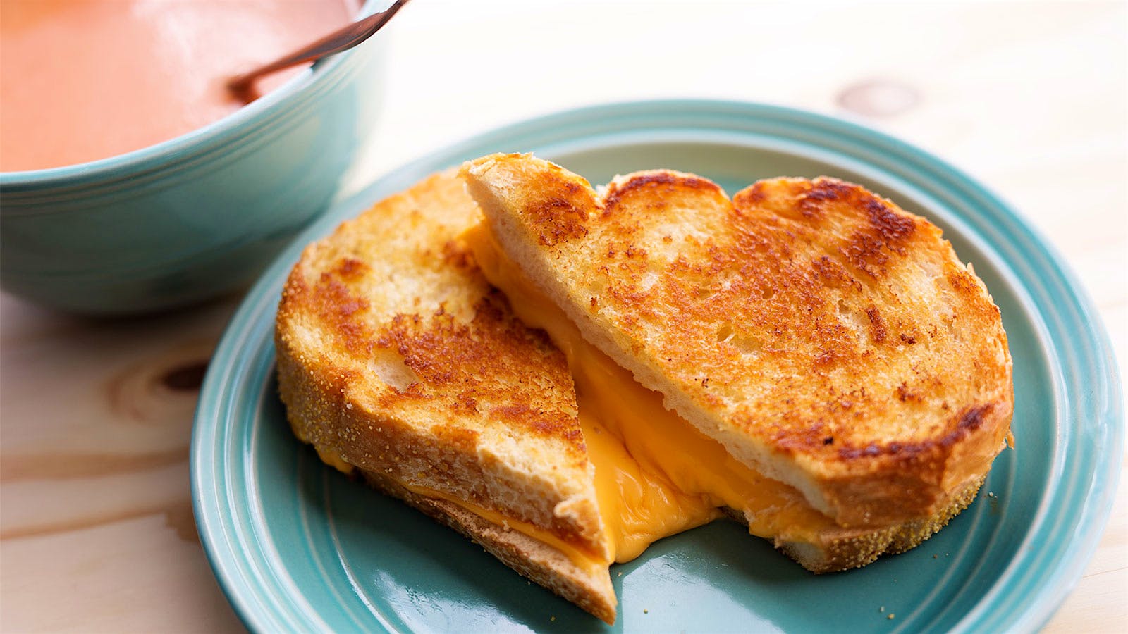  A grilled cheese sandwhich on a light blue plate with a light blue bowl holding cream of tomato soup