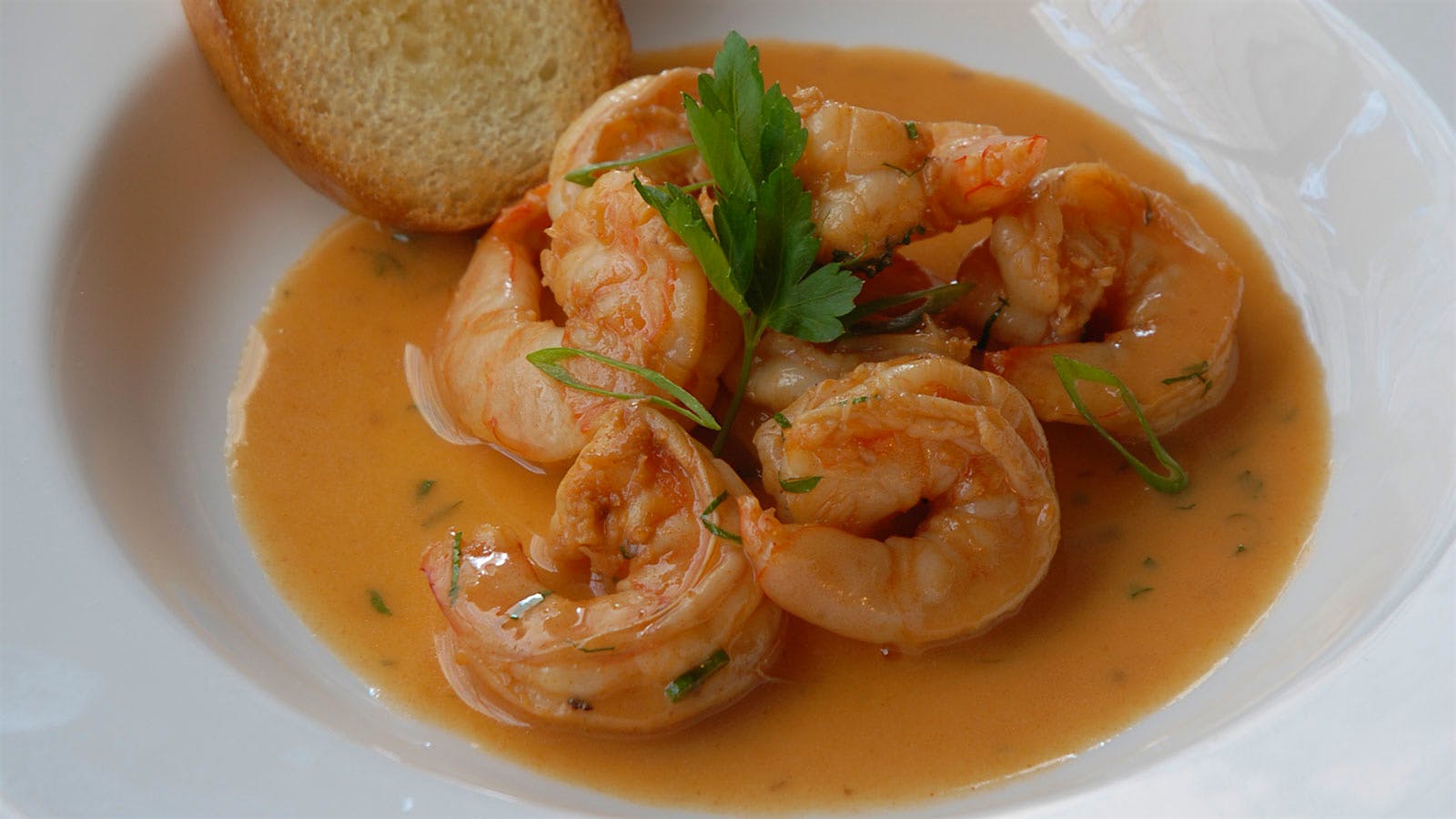 A bowl of shrimp in spicy butter sauce with a slice of bread on the side