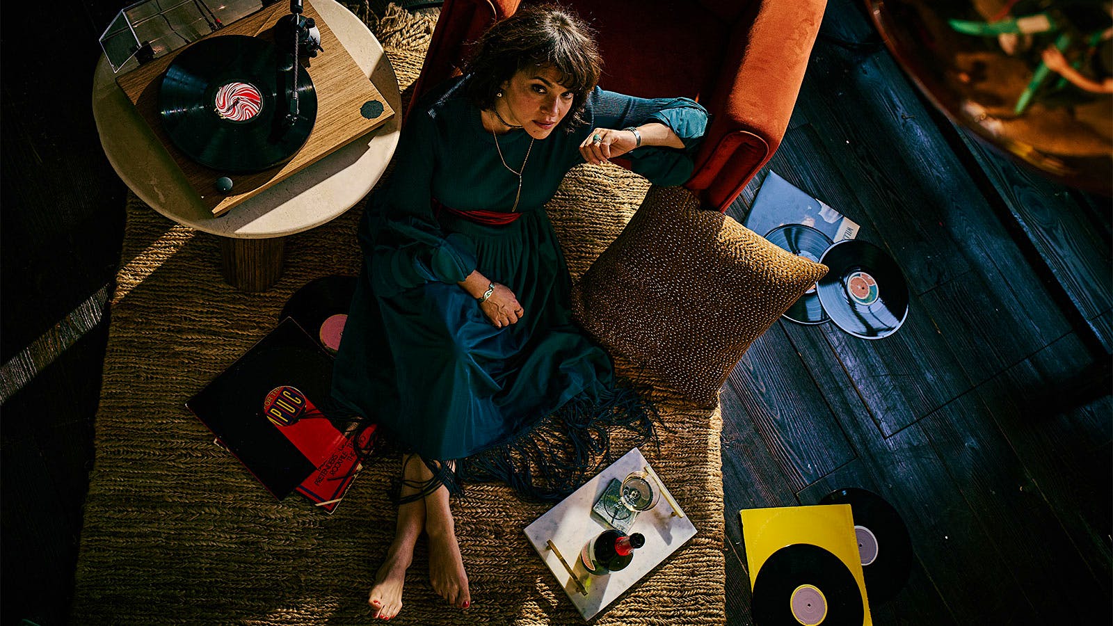  Singer Norah Jones reclining on a chair surrounded by records with a glass and bottle of wine at her side