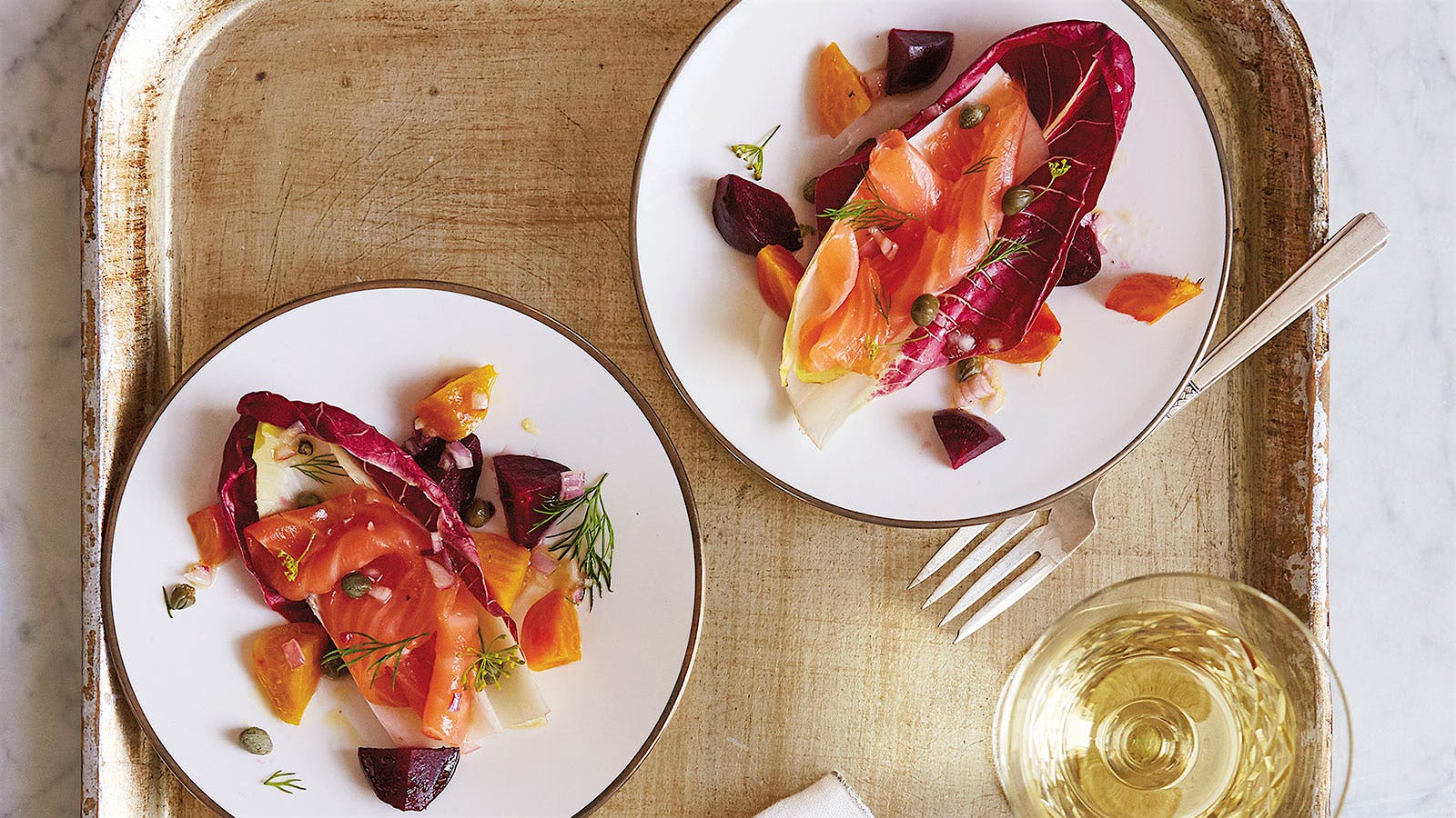 A salad made from smoked salmon, radicchio, endive, dill and beets is displayed alside a glass of white wine.