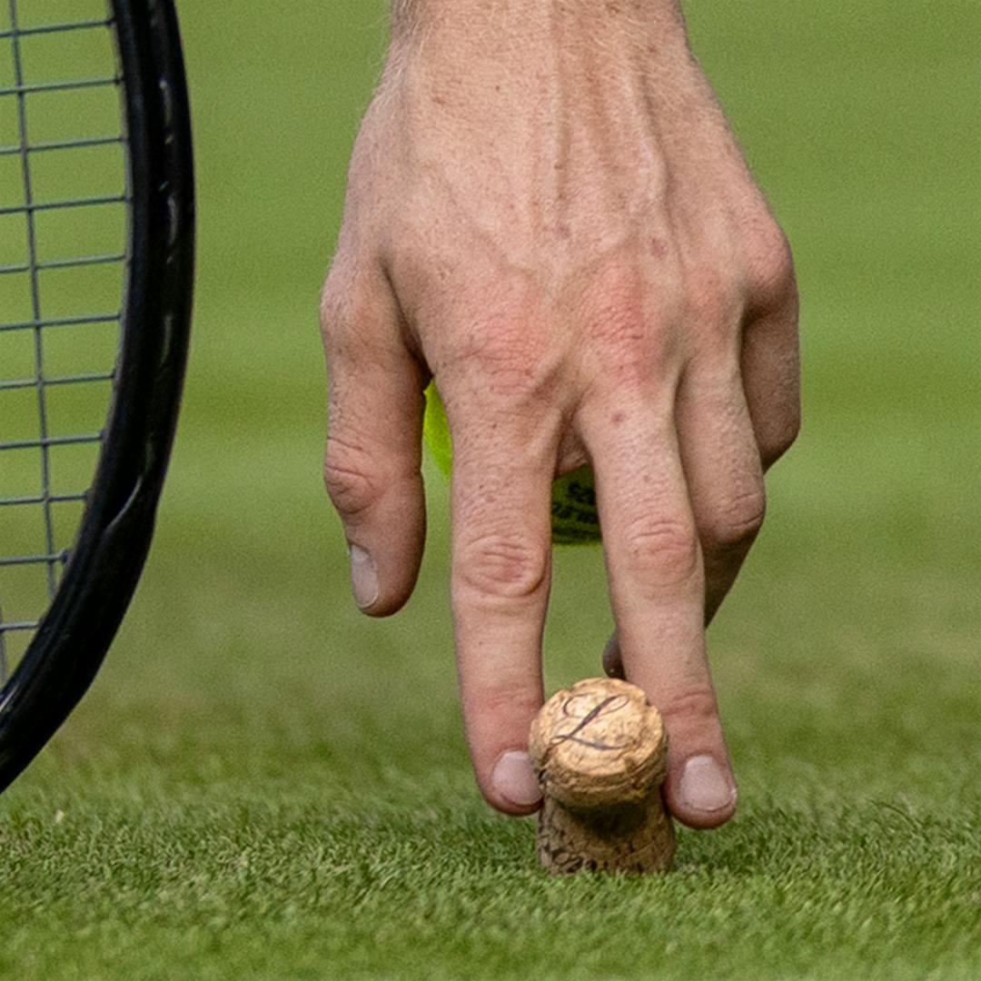 Tennis wunderkind Jannik Sinner picks a Champagne cork up off the grass at the 2025 Wimbledon final.