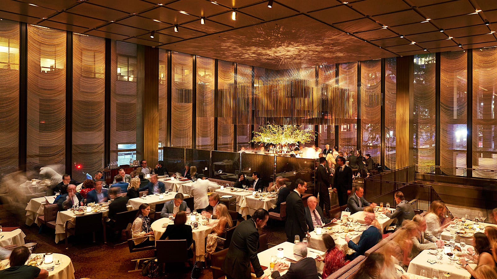  Diners in The Grill&rsquo;s contemporary design dining room, with plush fabric booths, leather-upholstered chairs, gold geometric chandeliers and a large window looking onto a neighboring building