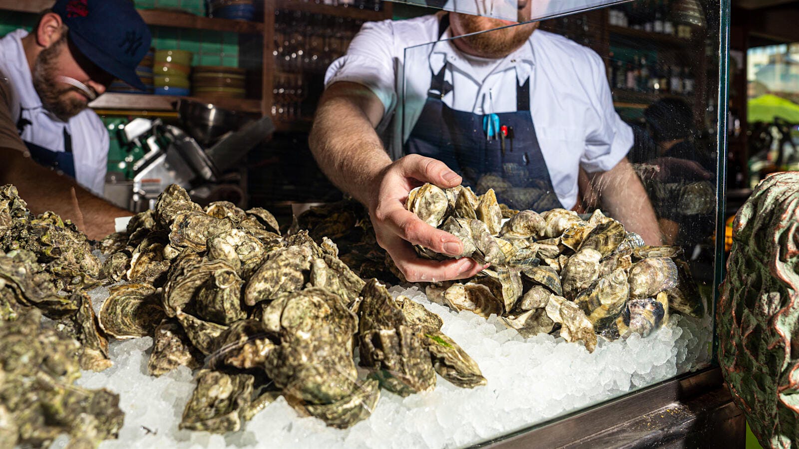 A restaurant worker grabs a pile of oysters off the top of a heap in a glass case at Mabel&rsquo;s Gone Fishing in San Diego, California.