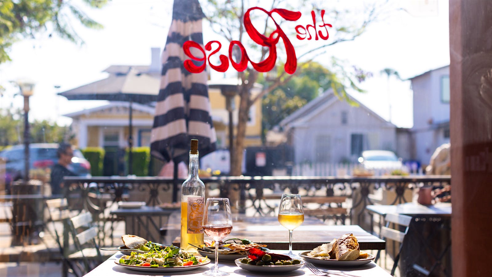 A table set with filled wine glasses, a bottle of wine and plates of food at The Rose wine bar in San Diego, California.