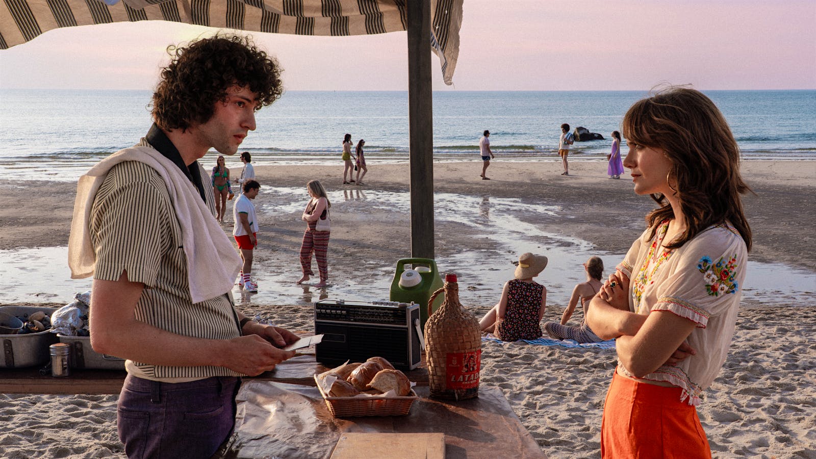  Still from the Anthony Bourdain biopic, “Tony” showing Dominic Sessa and Emilia Jones on the beach.