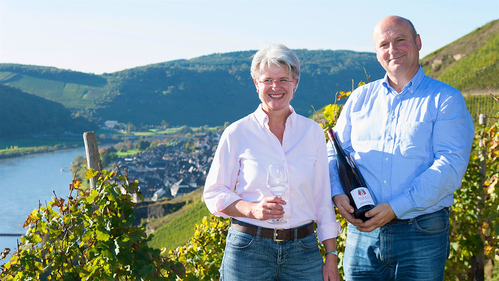 Barbara and Johannes Selbach standing in their vineyard, while Johannes holds a bottle of wine